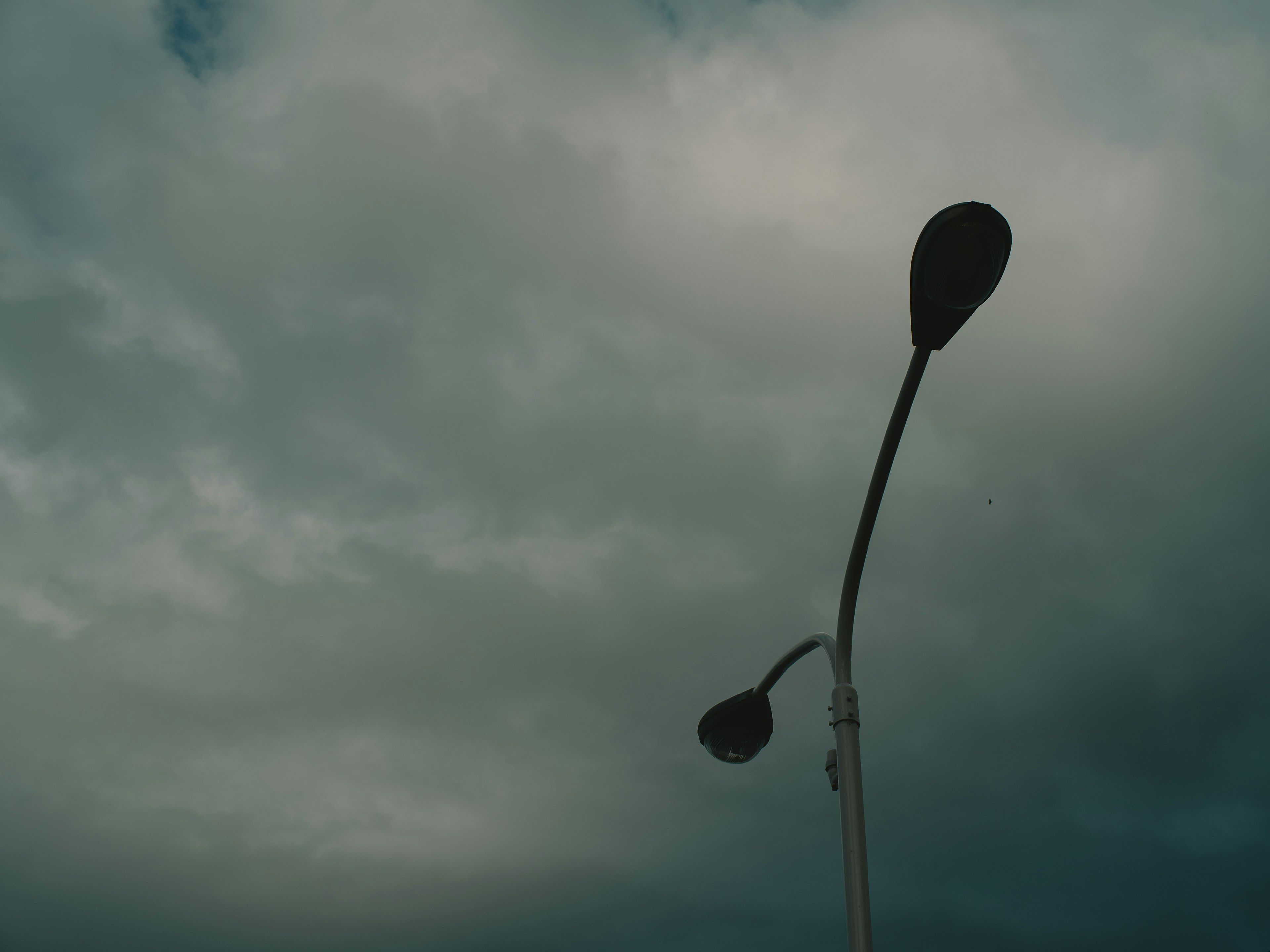 Silhouette of a streetlight under a cloudy sky