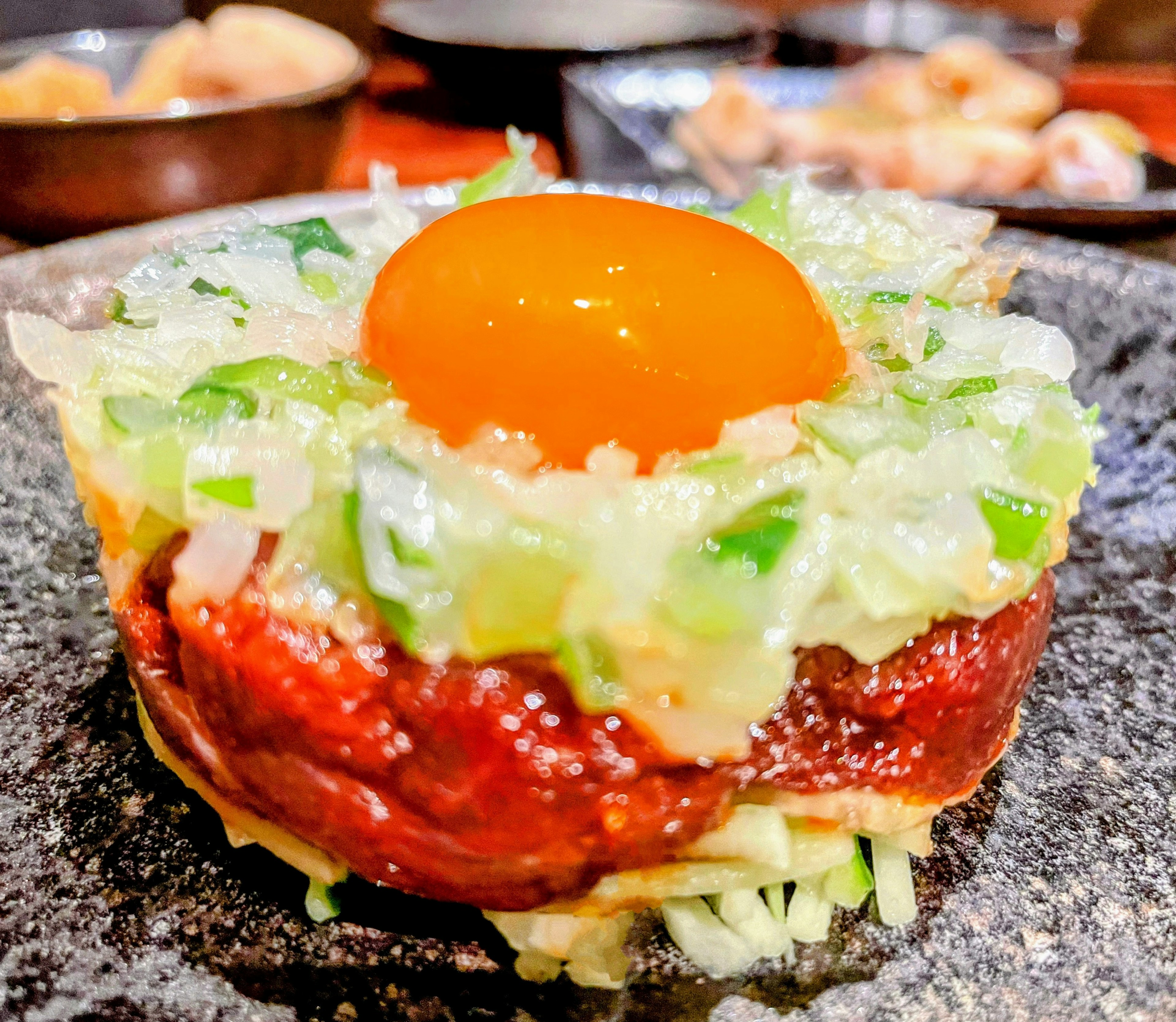 Una presentación de un plato de carne cubierto con yema de huevo y verduras finamente picadas