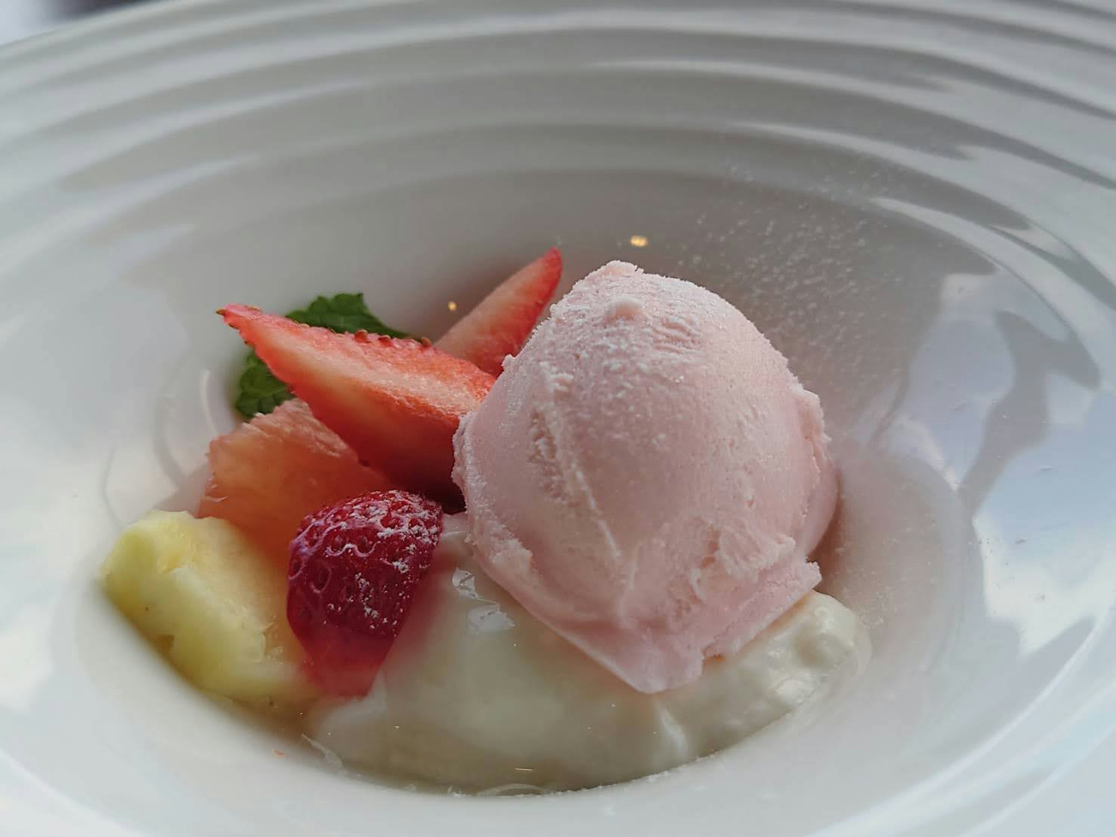 Dessert in a white bowl featuring pink ice cream topped with fresh fruits