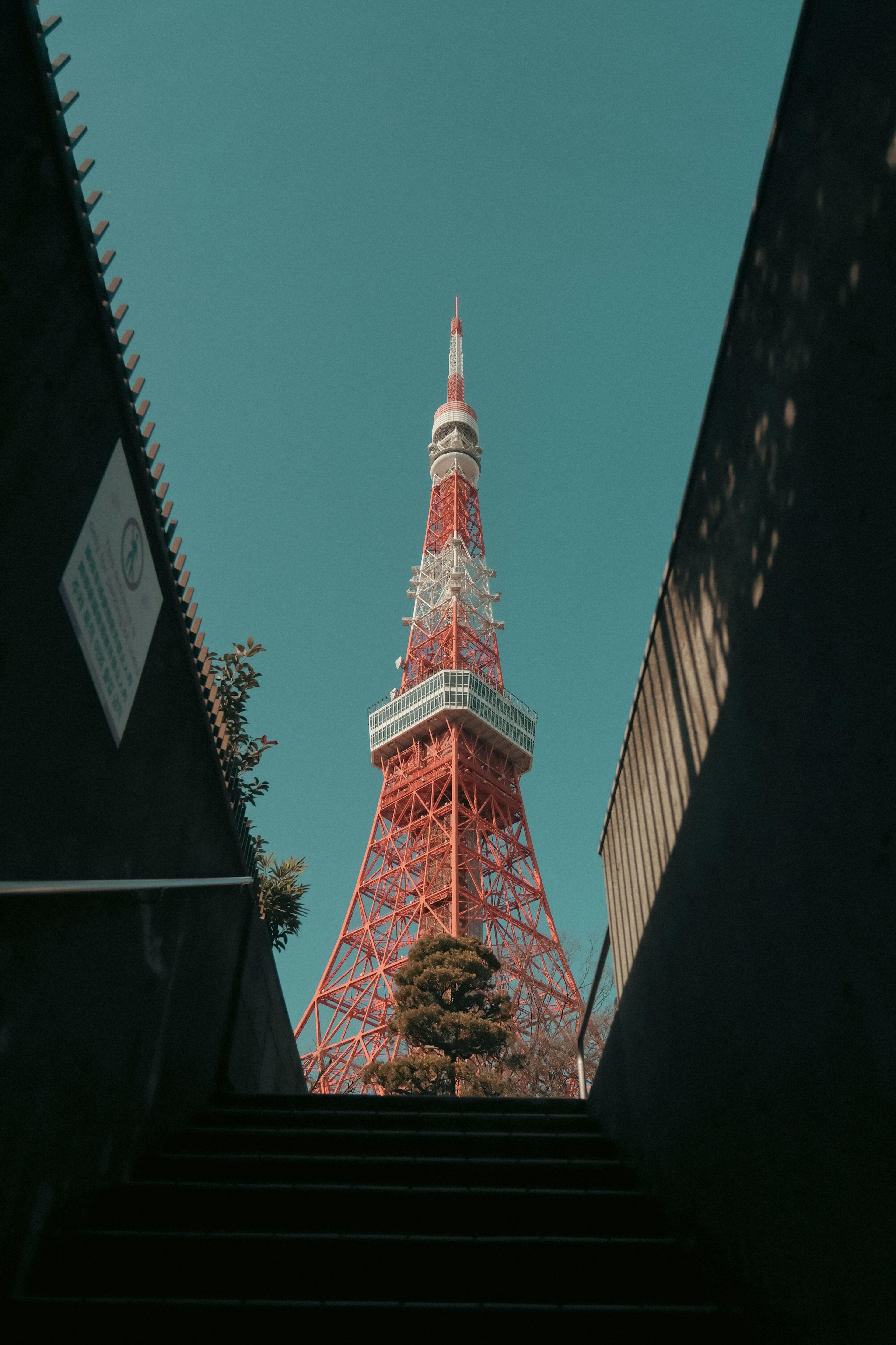 View of Tokyo Tower from the bottom of a staircase with a clear blue sky