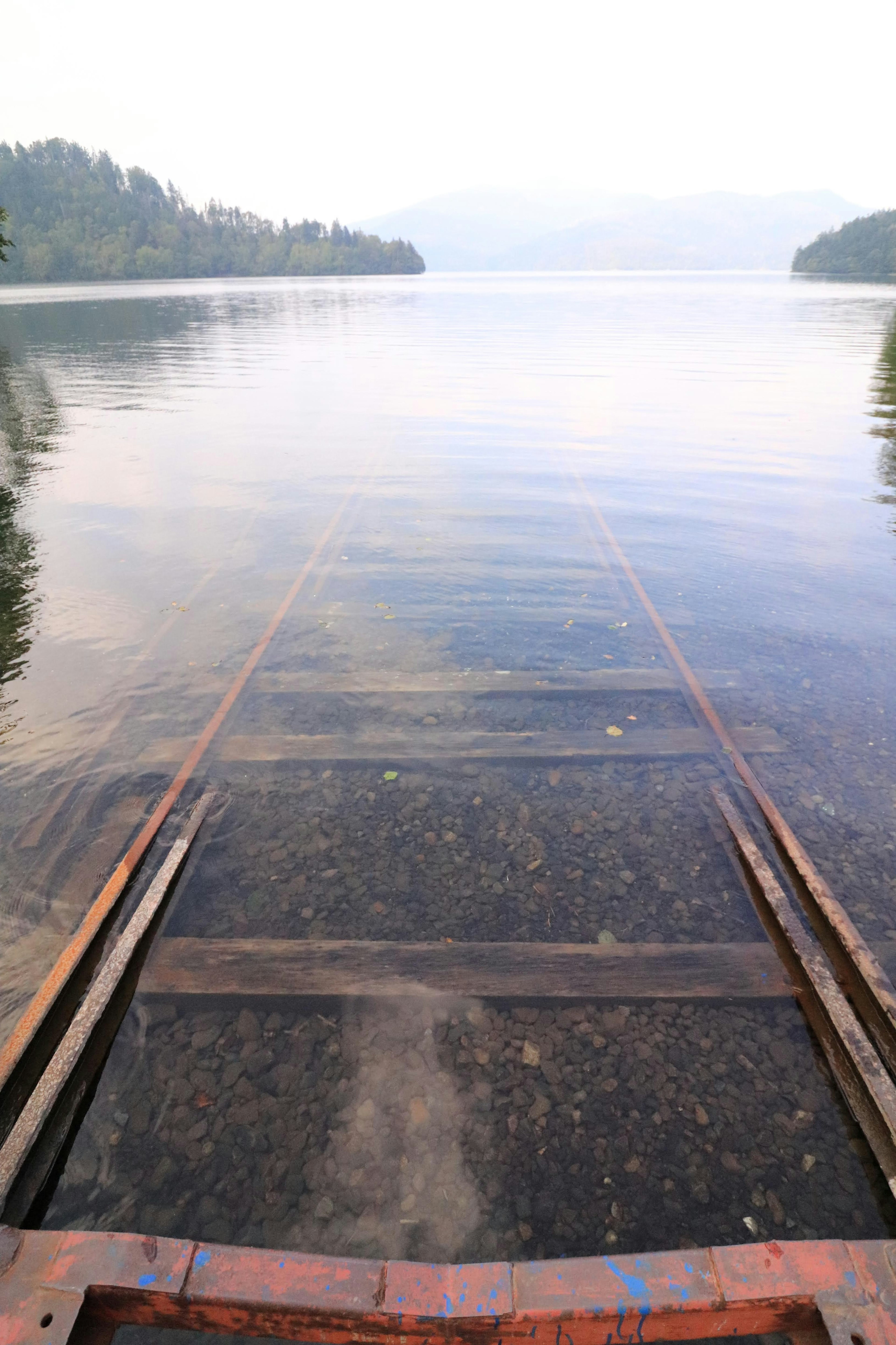 Alter Steg teilweise im ruhigen See untergetaucht, der die umliegende Landschaft spiegelt