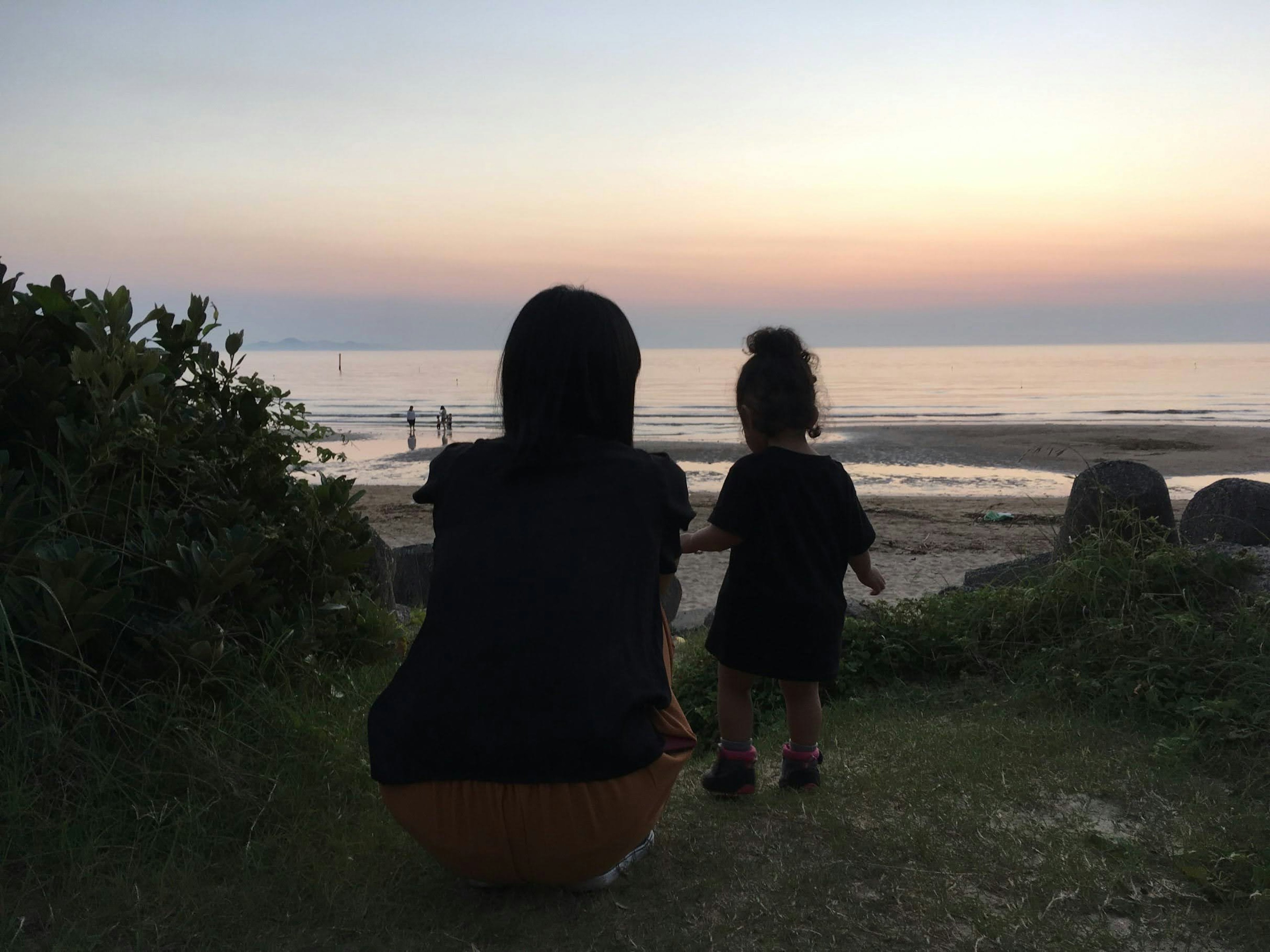 Silhouette einer Mutter und eines Kindes, die den Sonnenuntergang am Meer beobachten