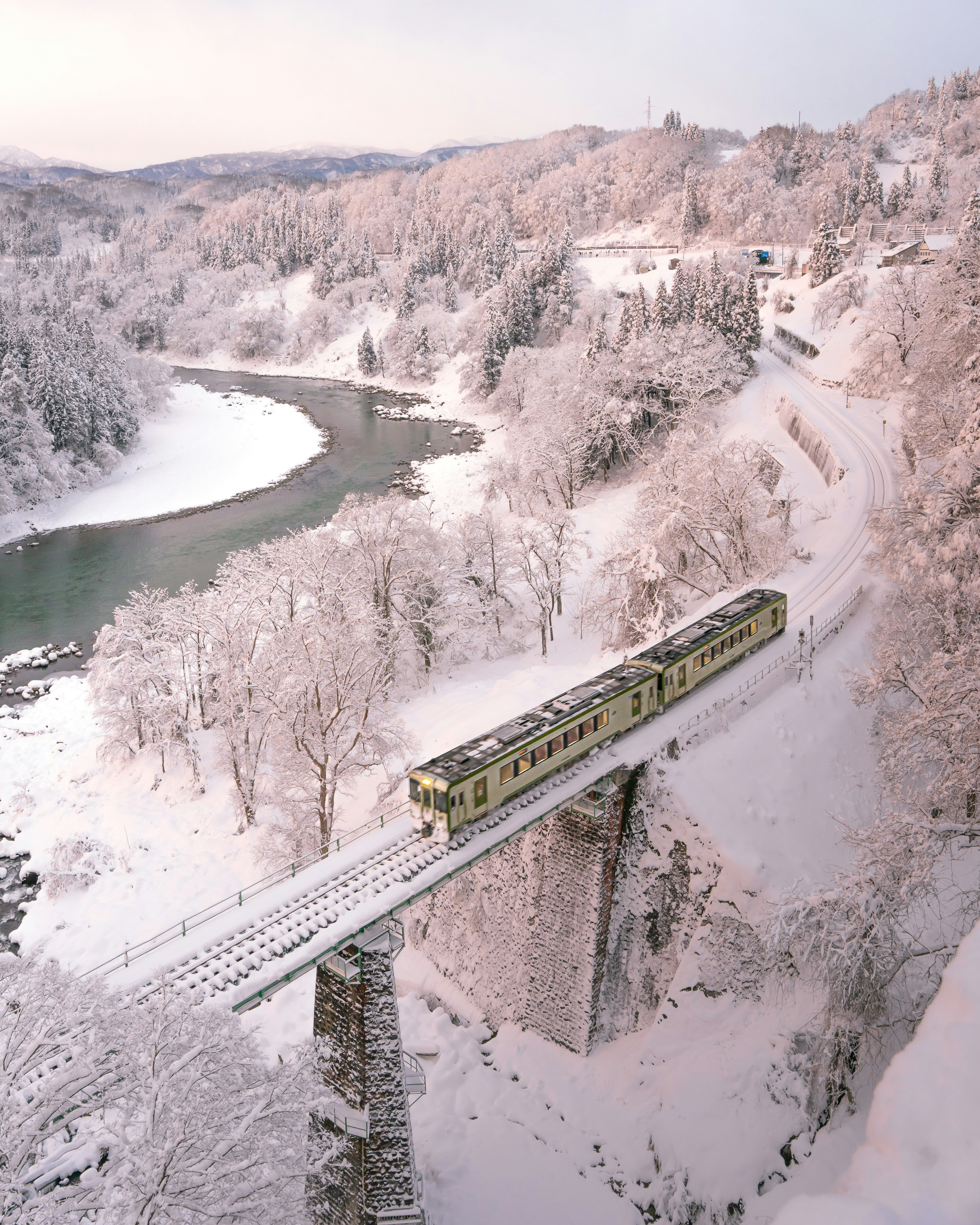 ทิวทัศน์สวยงามของรถไฟที่ข้ามสะพานที่มีหิมะเหนือแม่น้ำ