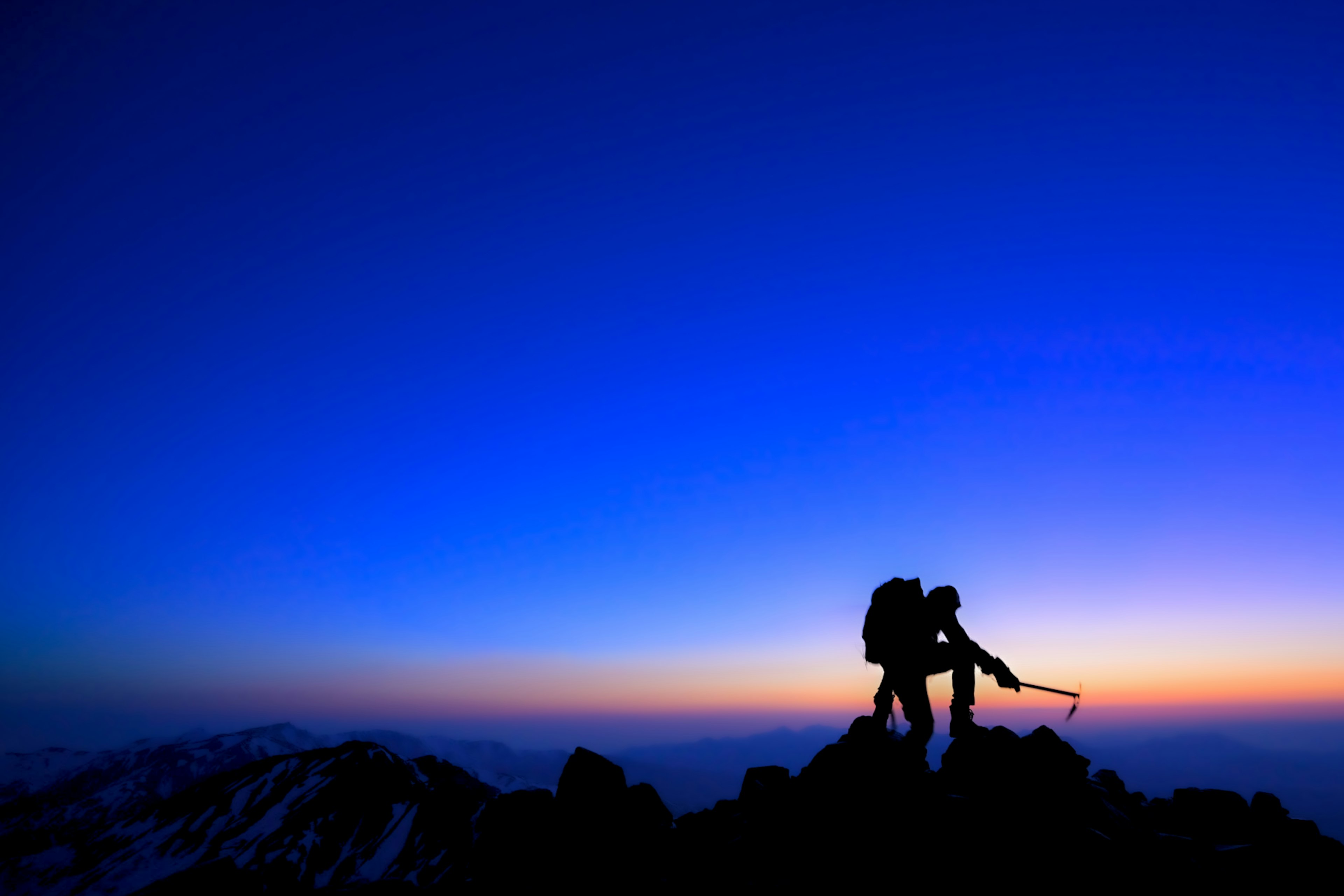 Deux grimpeurs silhouettés contre un ciel crépusculaire au sommet de la montagne