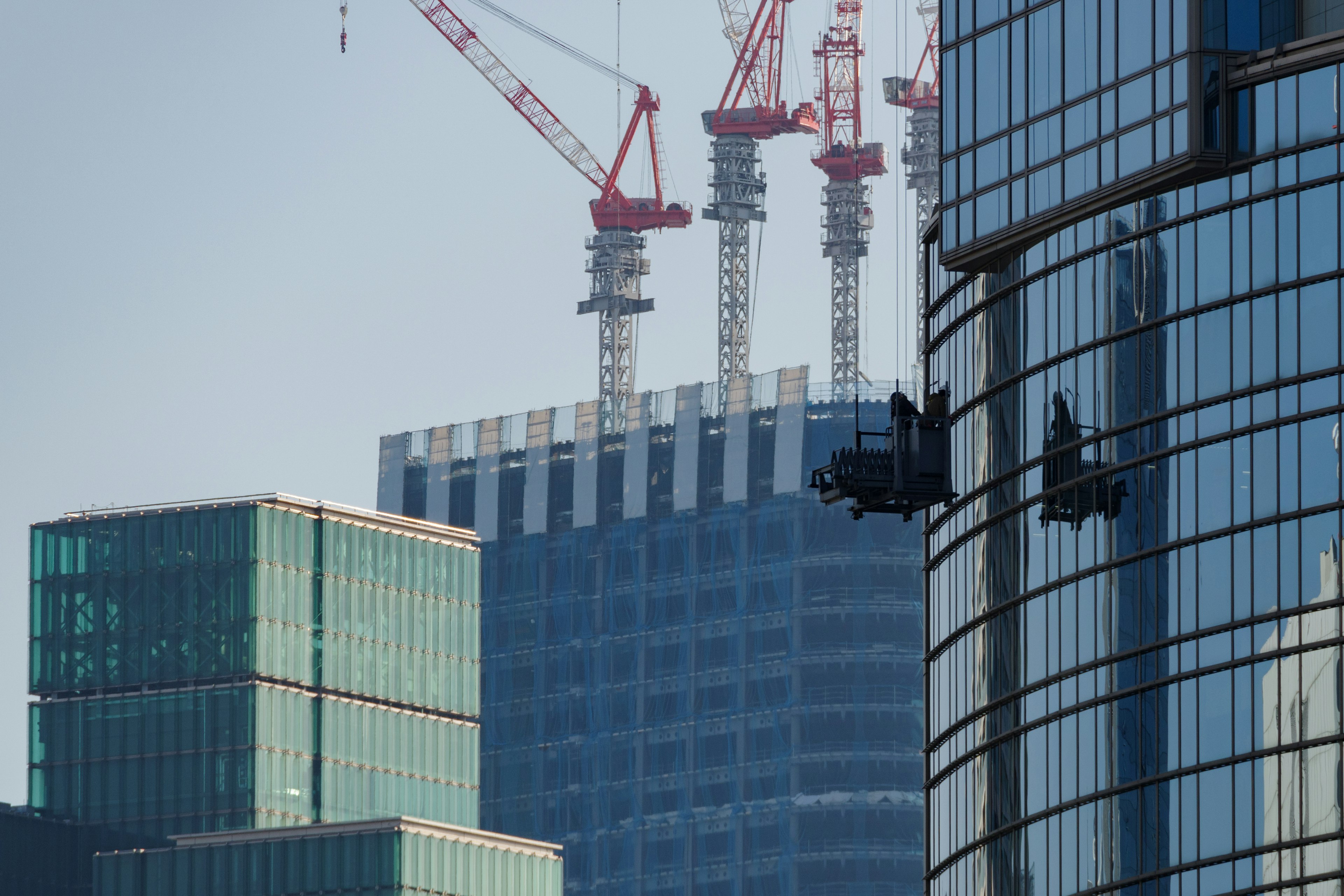 Travailleurs nettoyant les fenêtres des gratte-ciels avec des grues de construction en arrière-plan