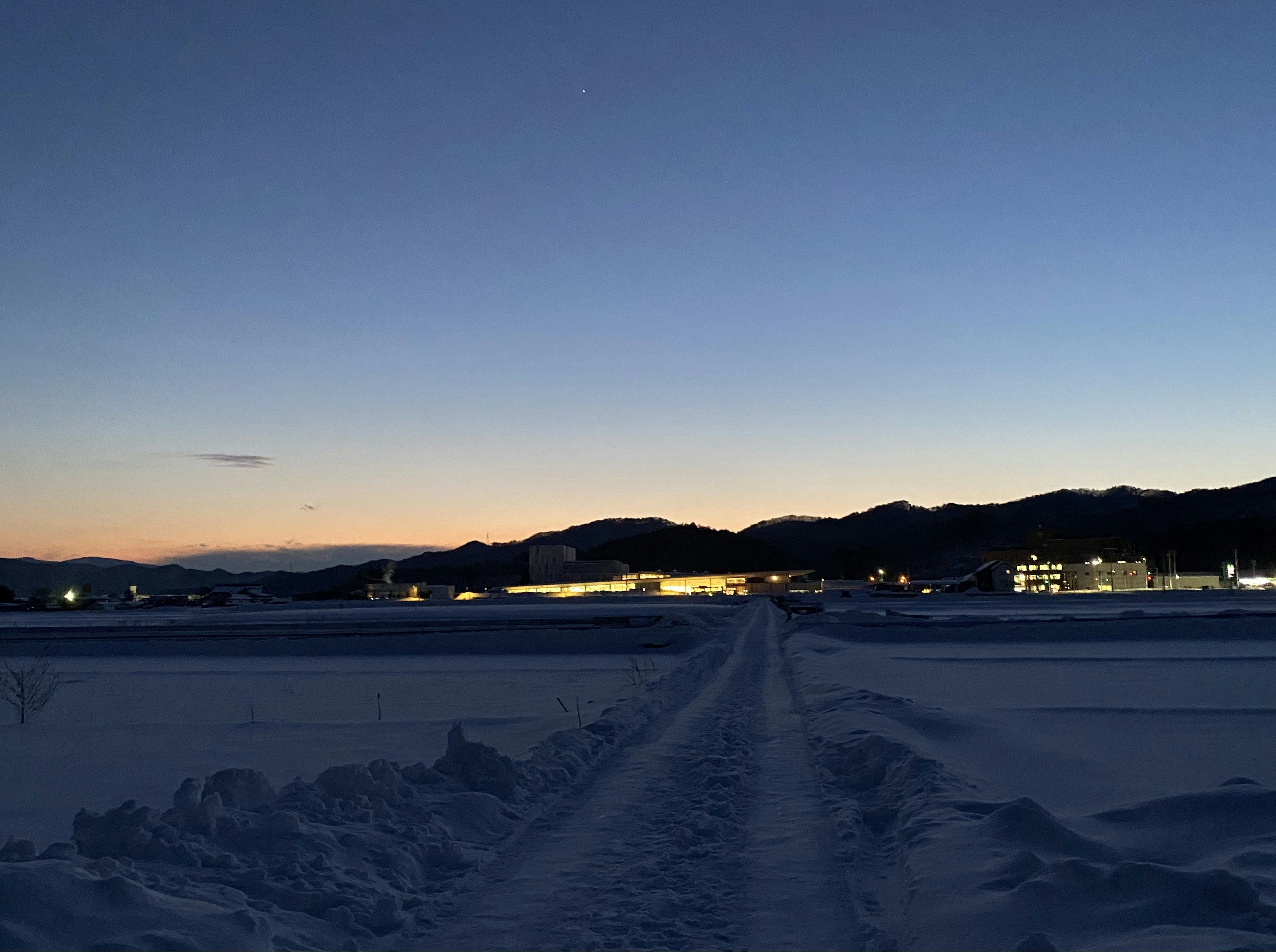 雪に覆われた道と山のシルエットが広がる夕暮れの風景