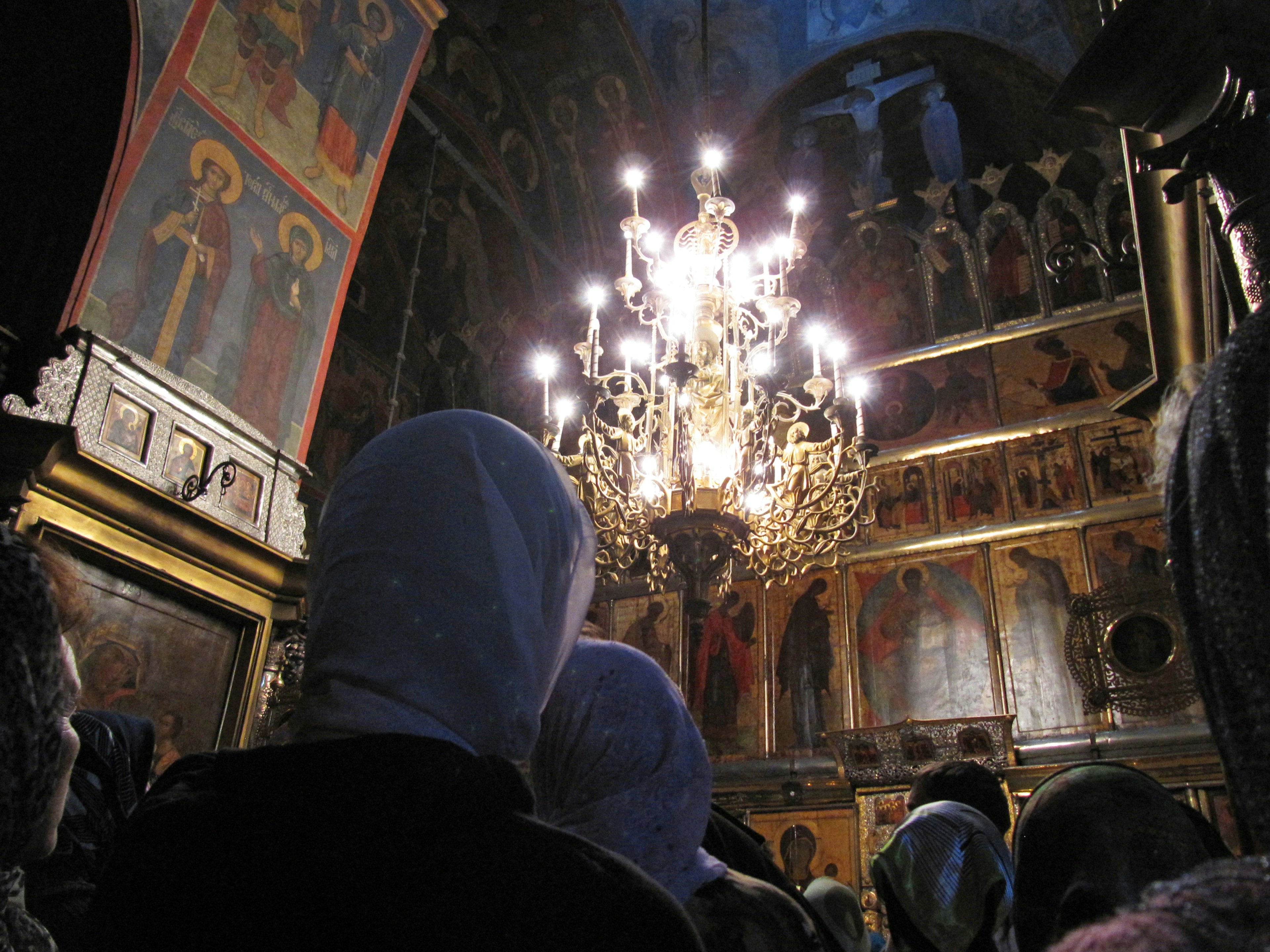 Innenraum einer Kirche mit Menschen, die Kopftücher tragen, versammelt, Kronleuchterlichter erhellen den Raum