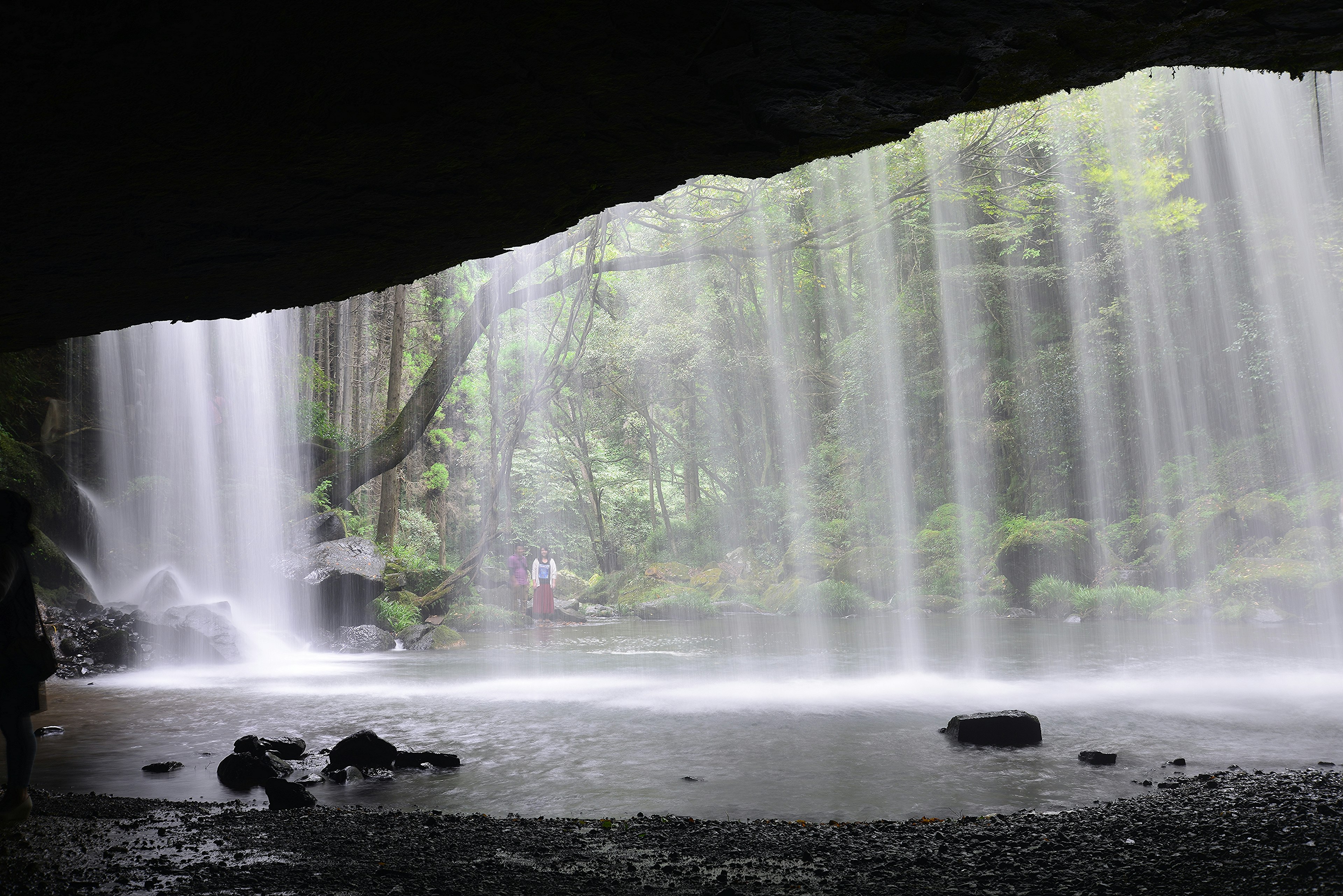 View of a lush green landscape and curtain of water from behind a waterfall