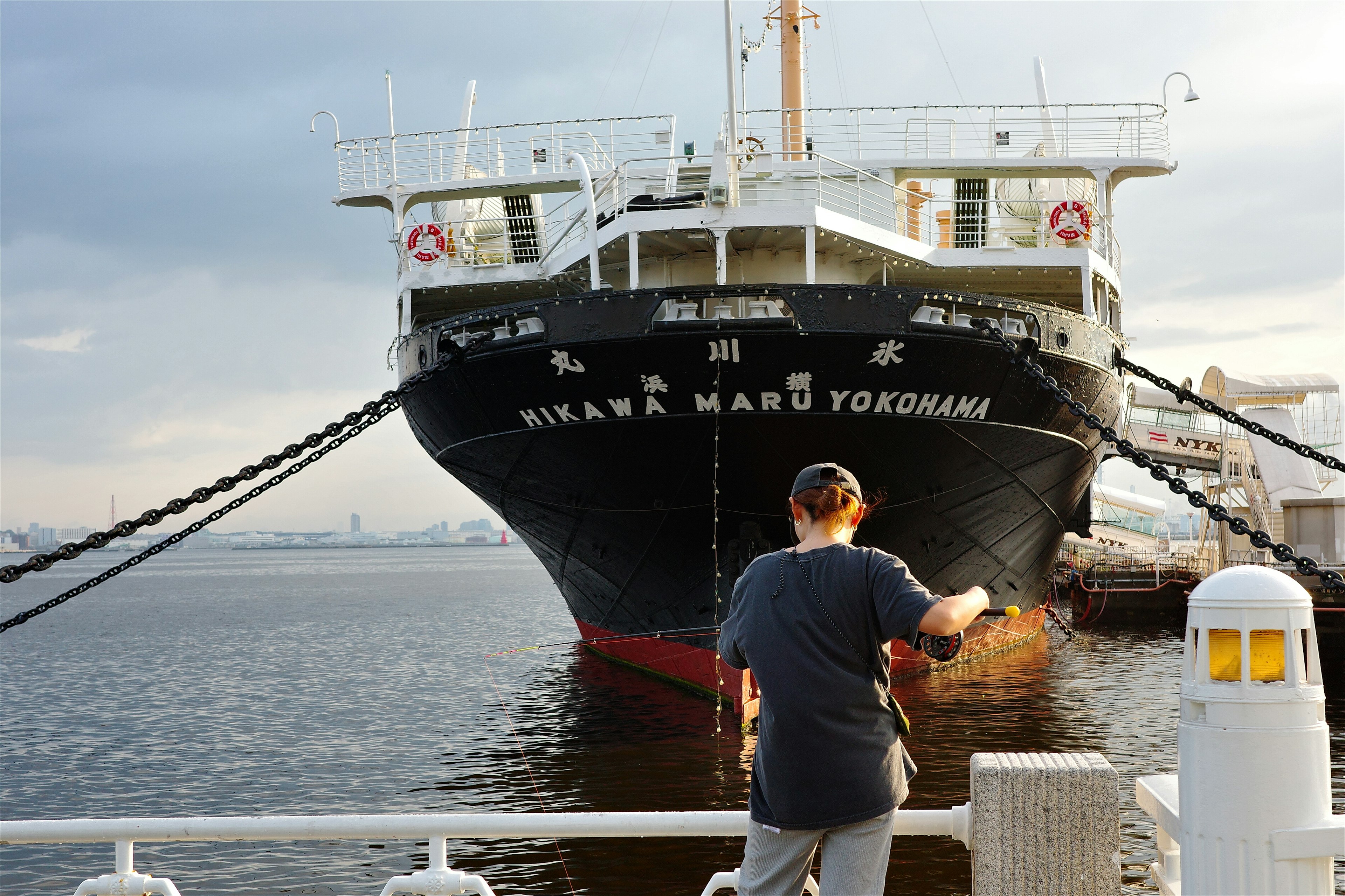 A person standing in front of a large ship docked at Yokohama Harbor