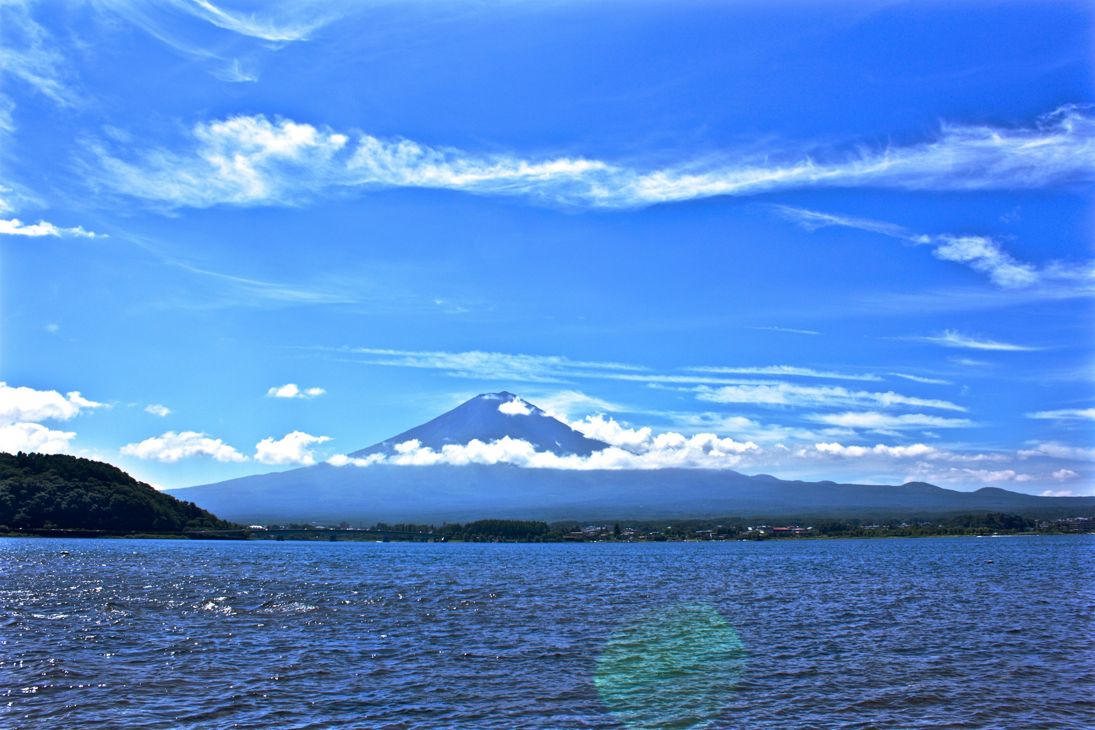 Vista del lago con il Monte Fuji sotto un cielo blu e nuvole bianche