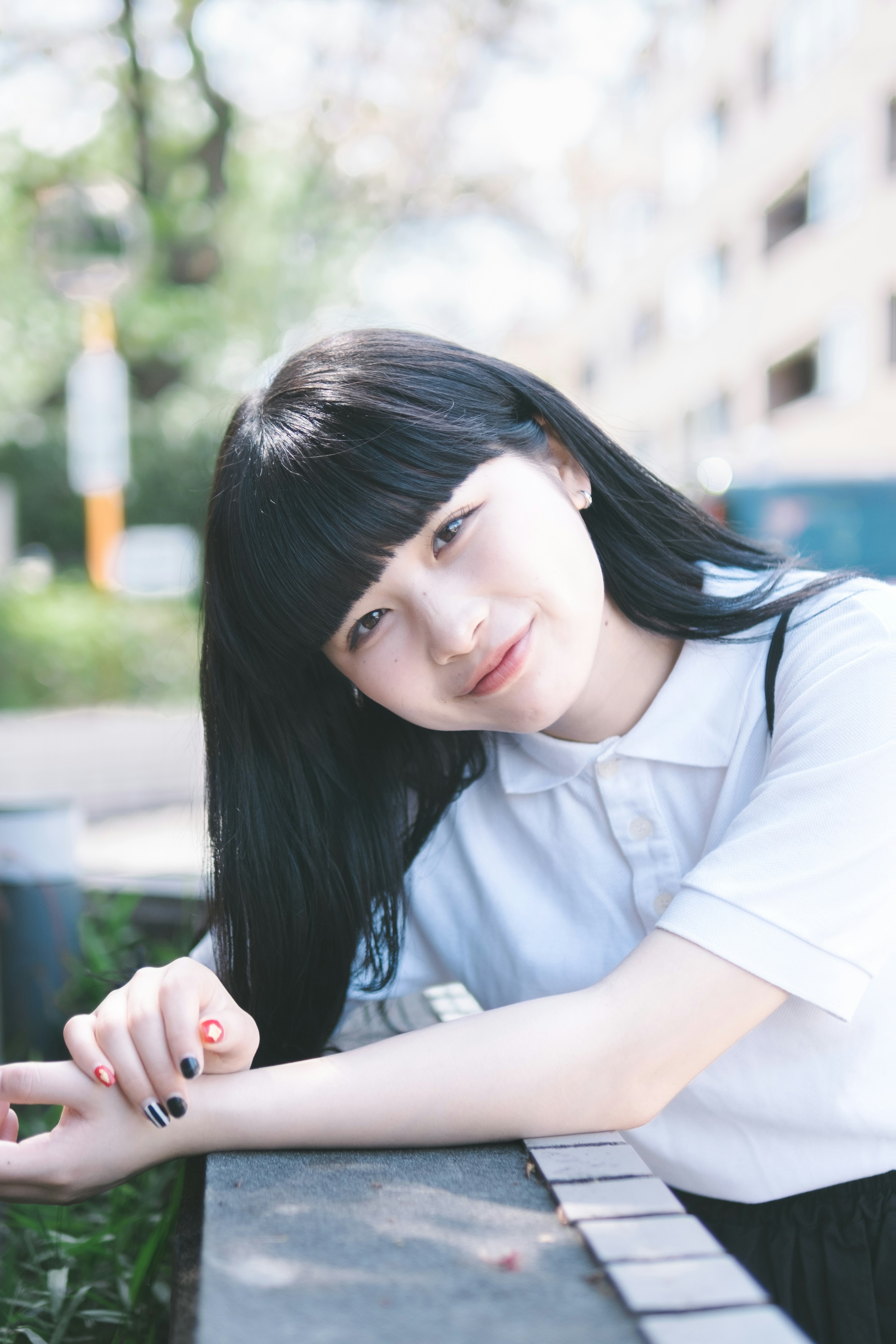 Young woman relaxing in a park, long black hair, white shirt, smiling