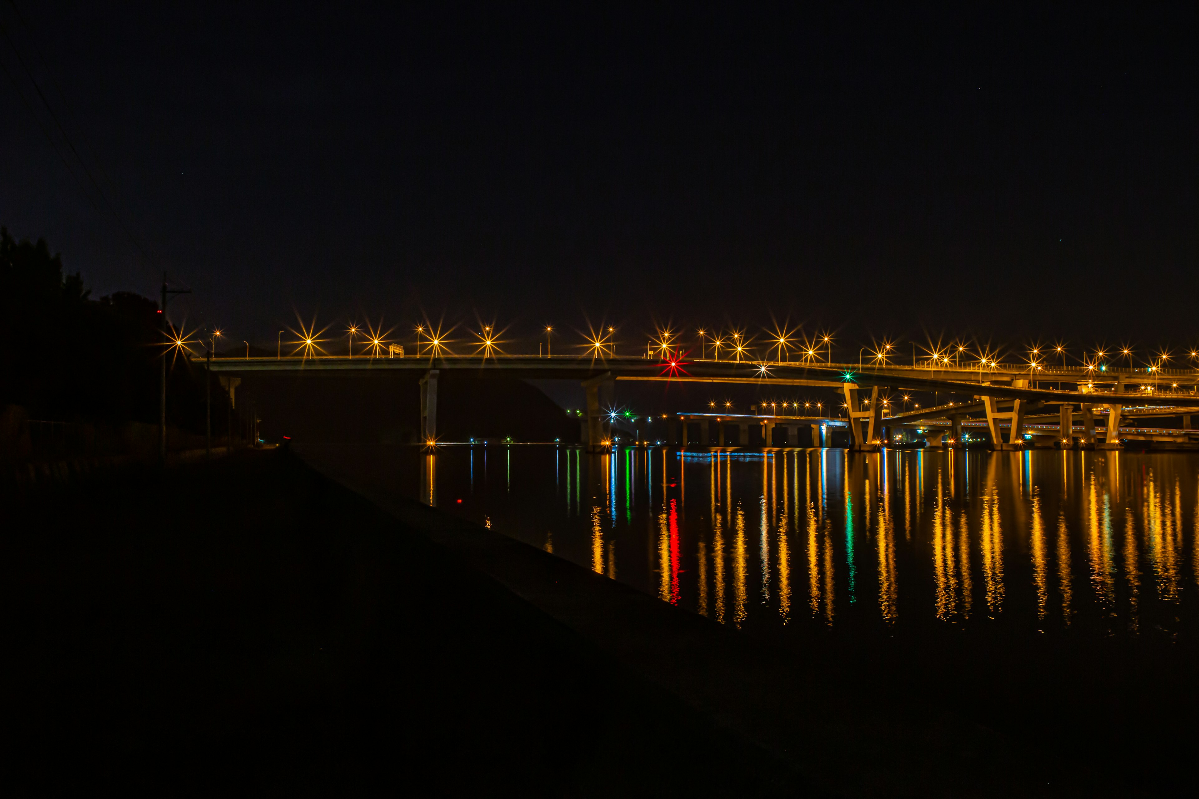 Jembatan terang yang memantulkan di sungai di malam hari