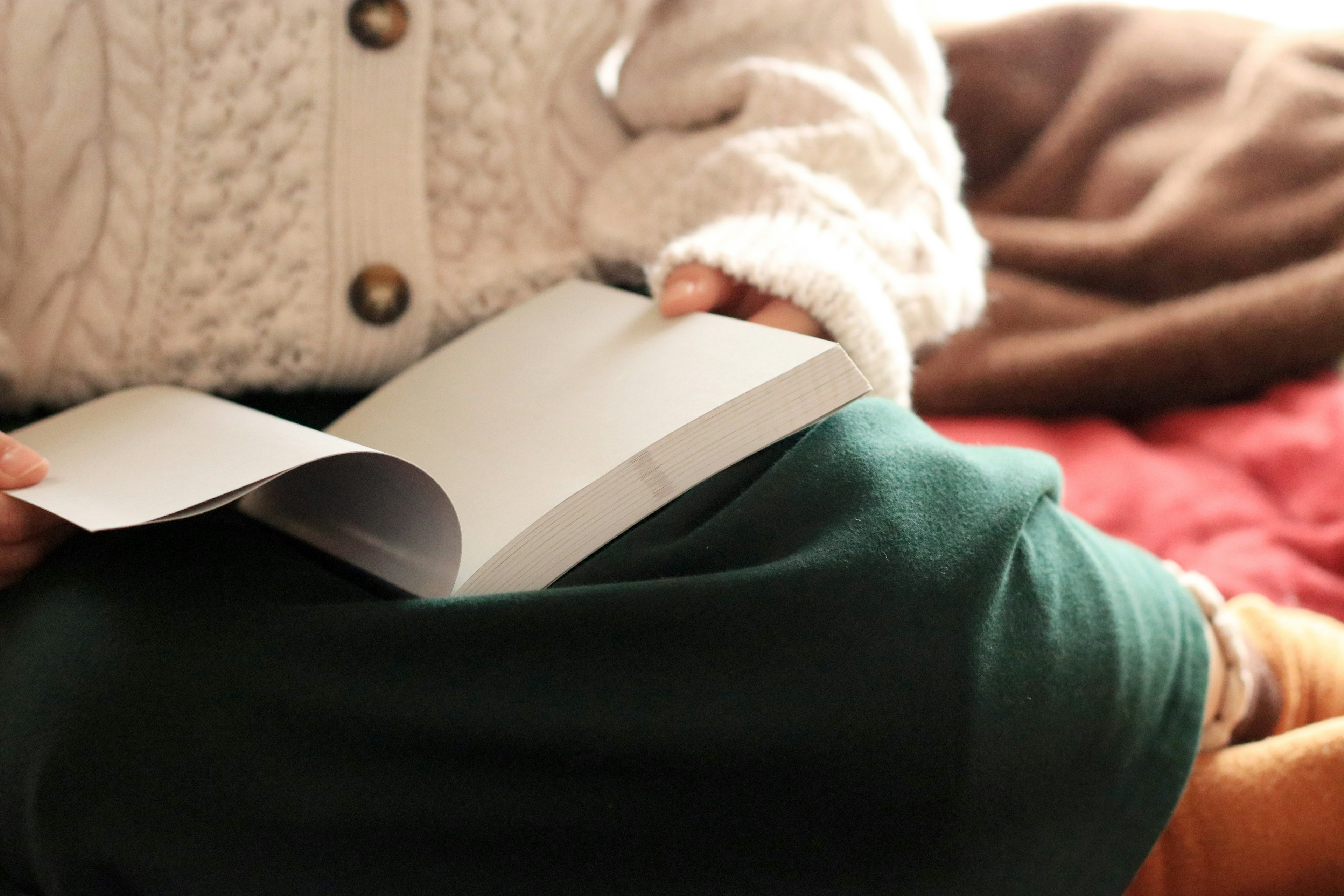 Niño con suéter cálido leyendo un libro en una cama acogedora