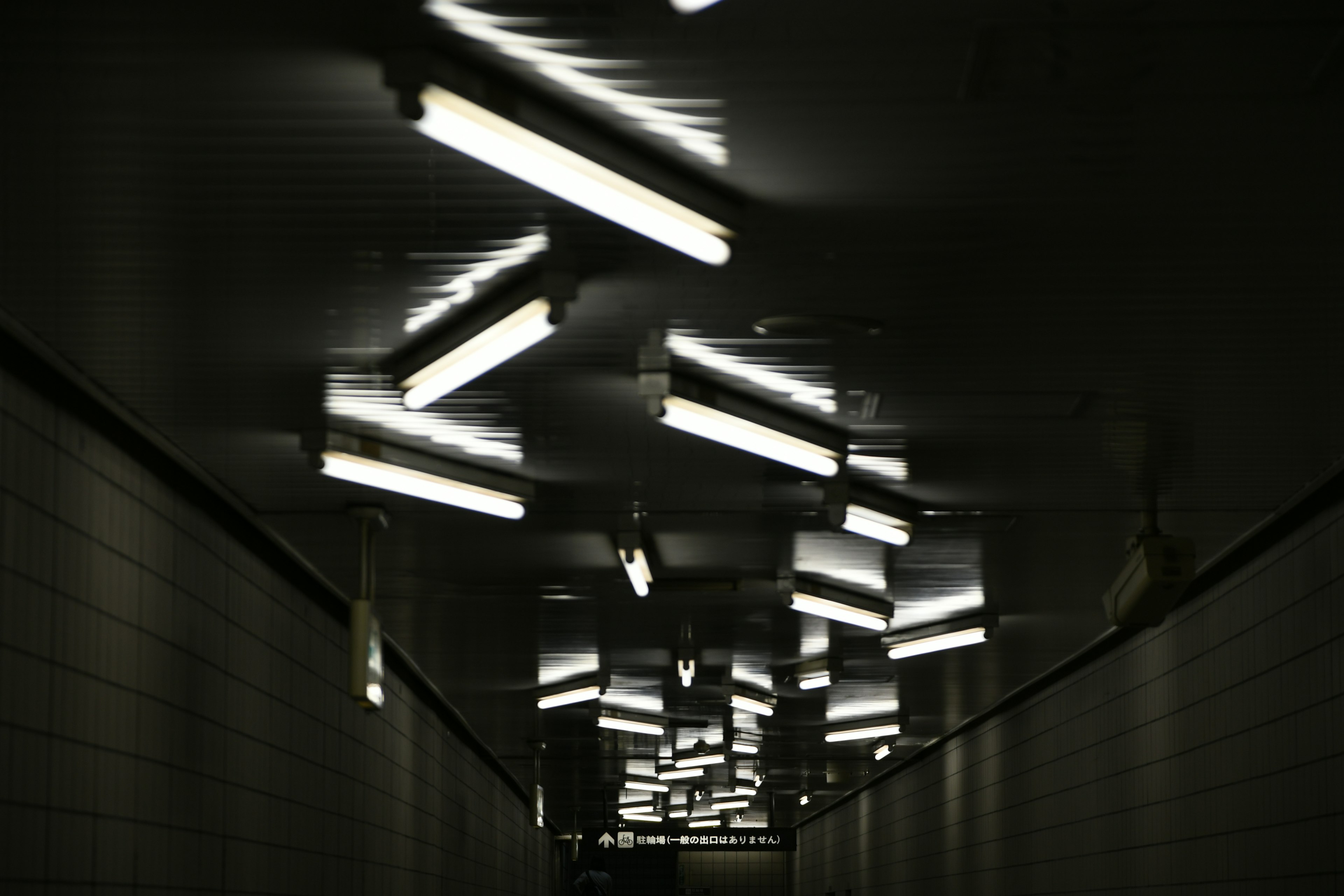 Dimly lit tunnel with bright fluorescent lights hanging from the ceiling