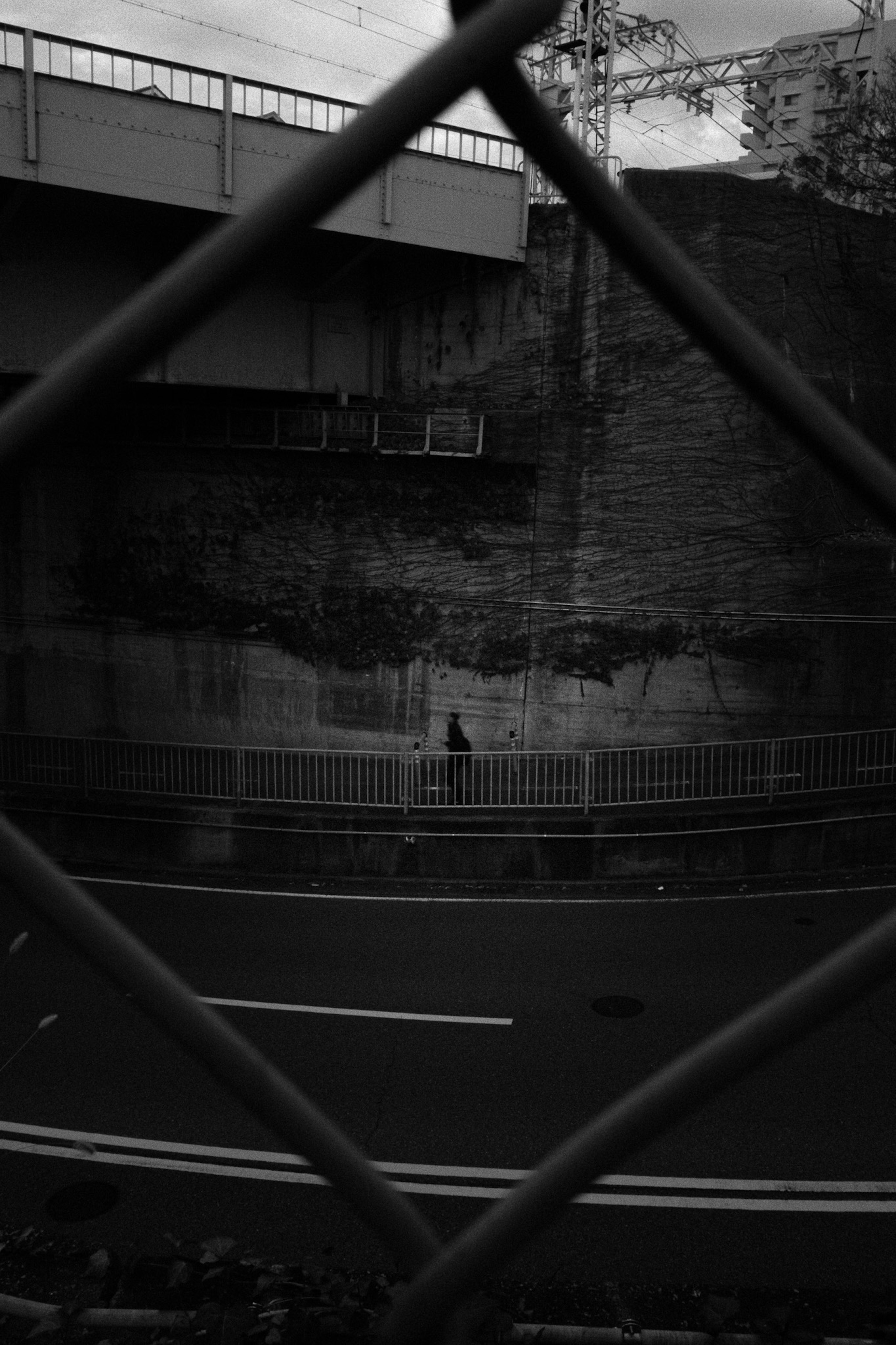 Black and white urban scene with a road and part of a building seen through a fence