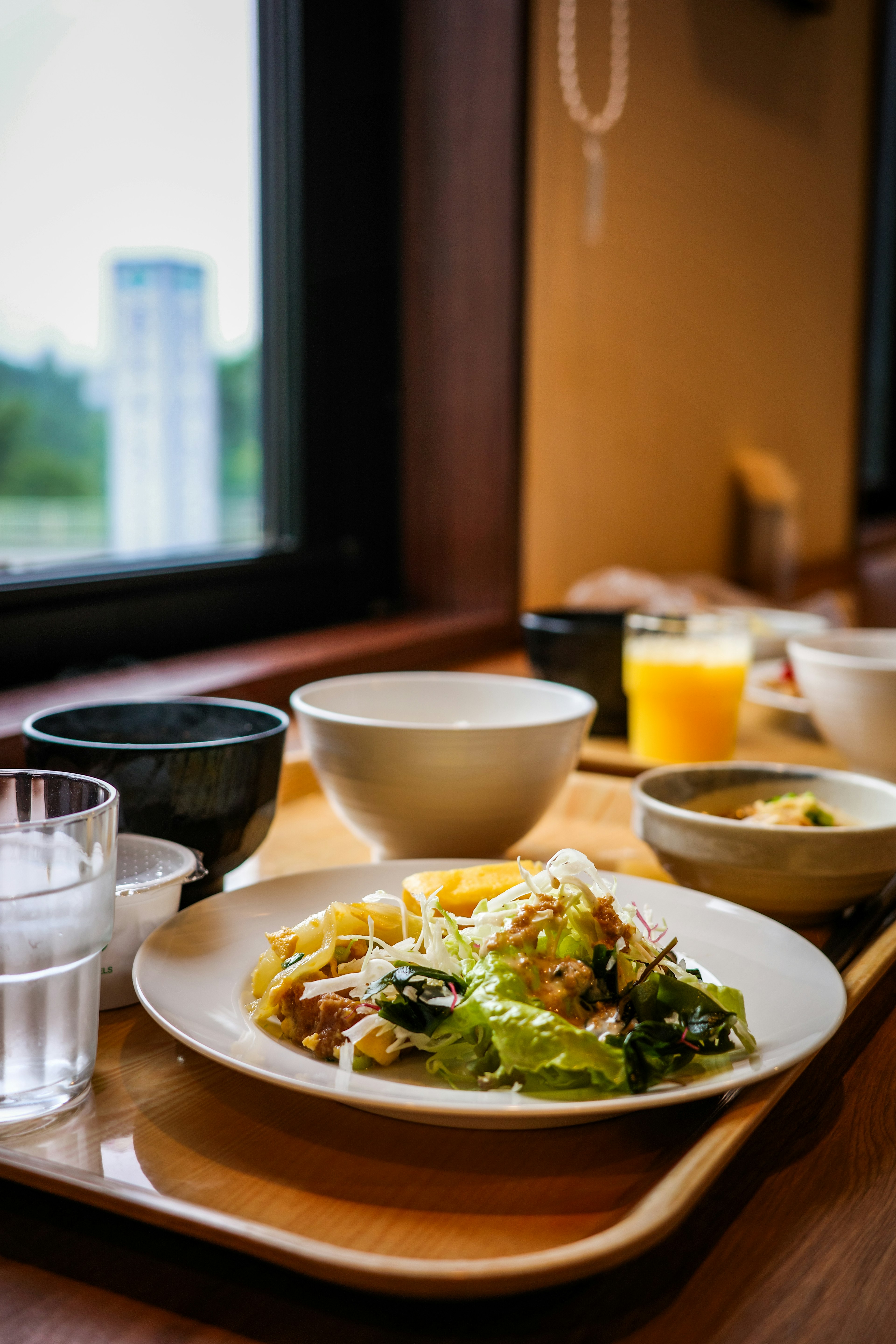 Meal set arranged on a table by the window Salad and vegetables on a white plate Clear glass and black bowl