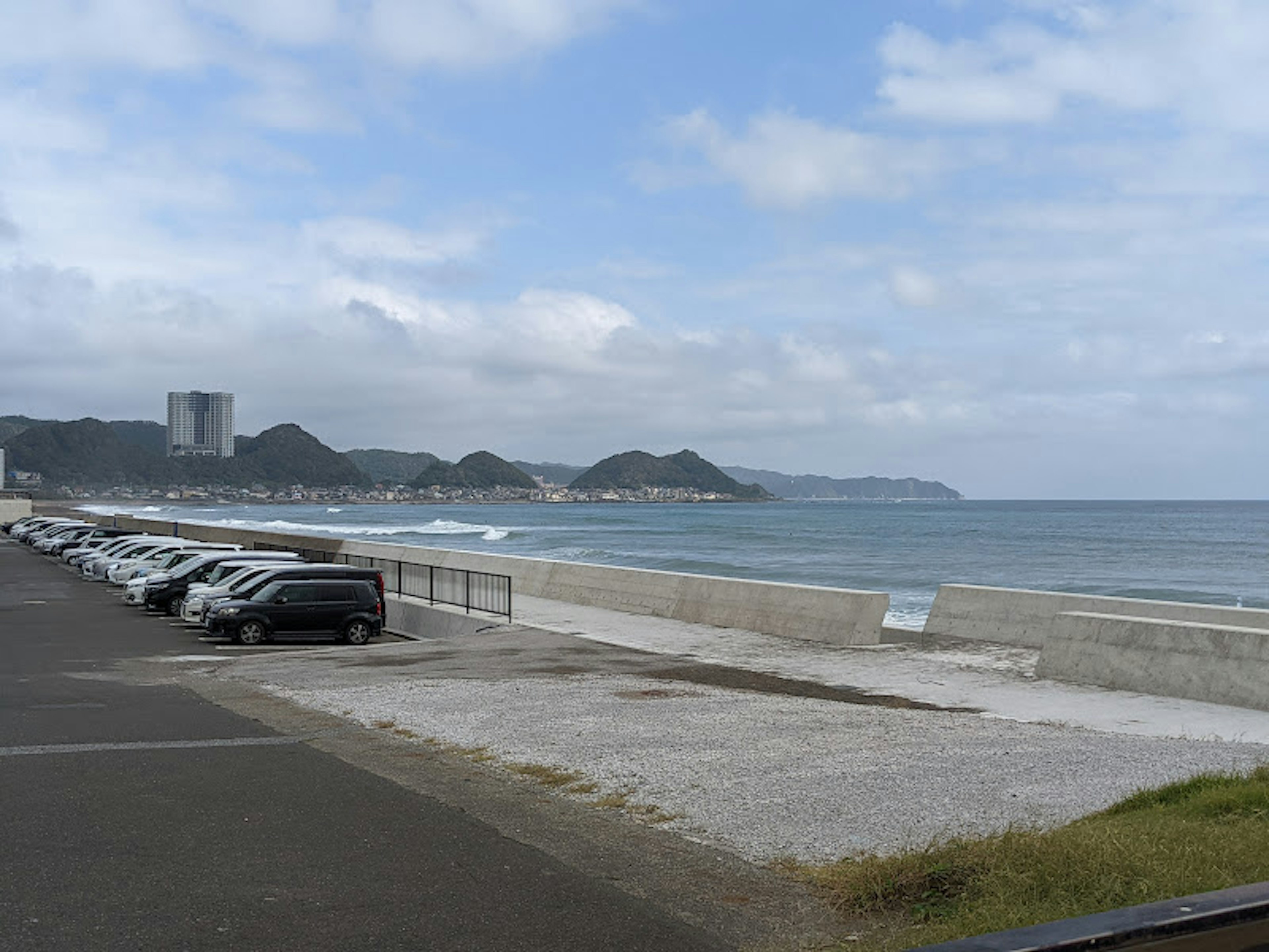 Vista costiera con auto parcheggiate e onde dolci con montagne sullo sfondo