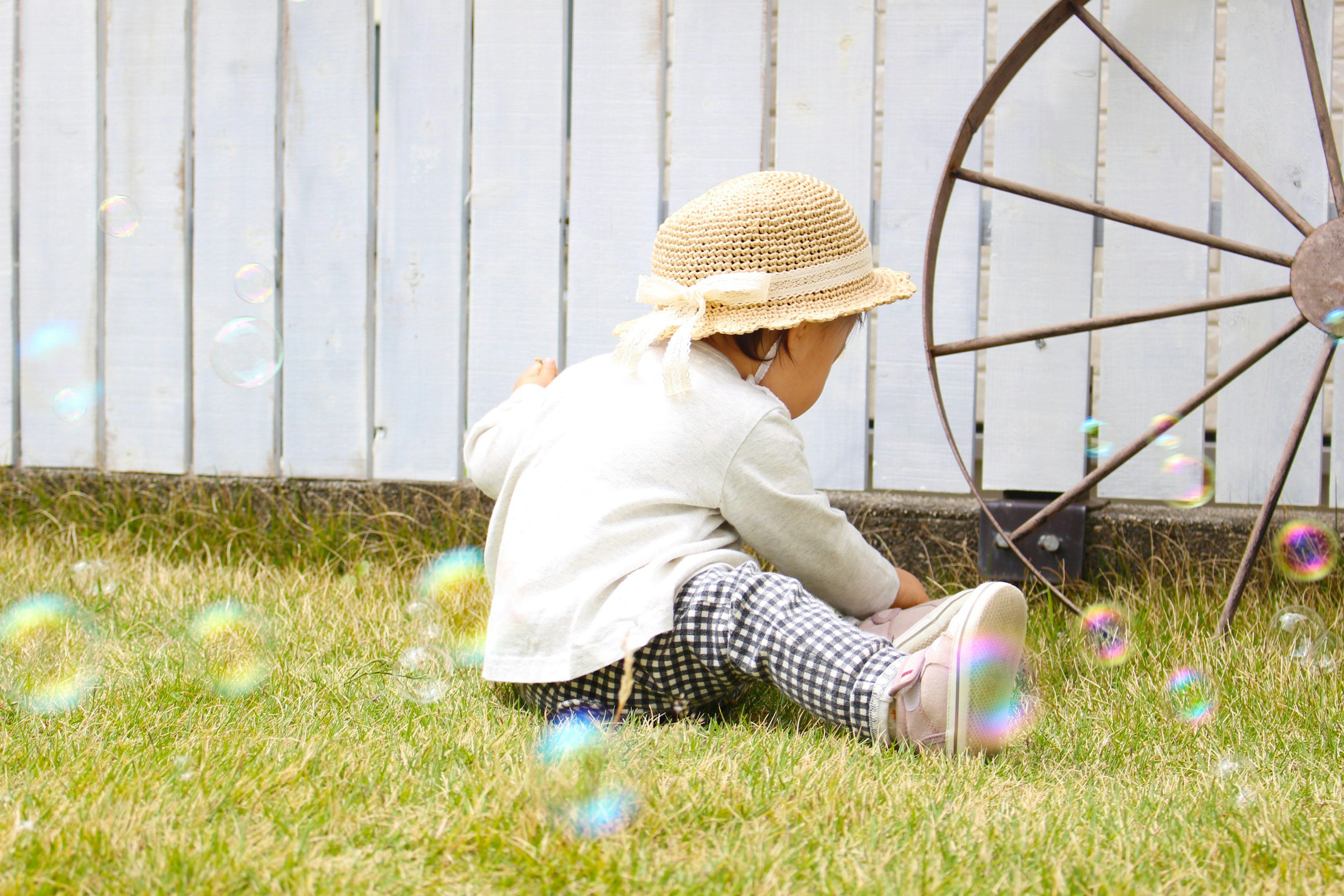 A child sitting on grass with a hat bubbles floating around