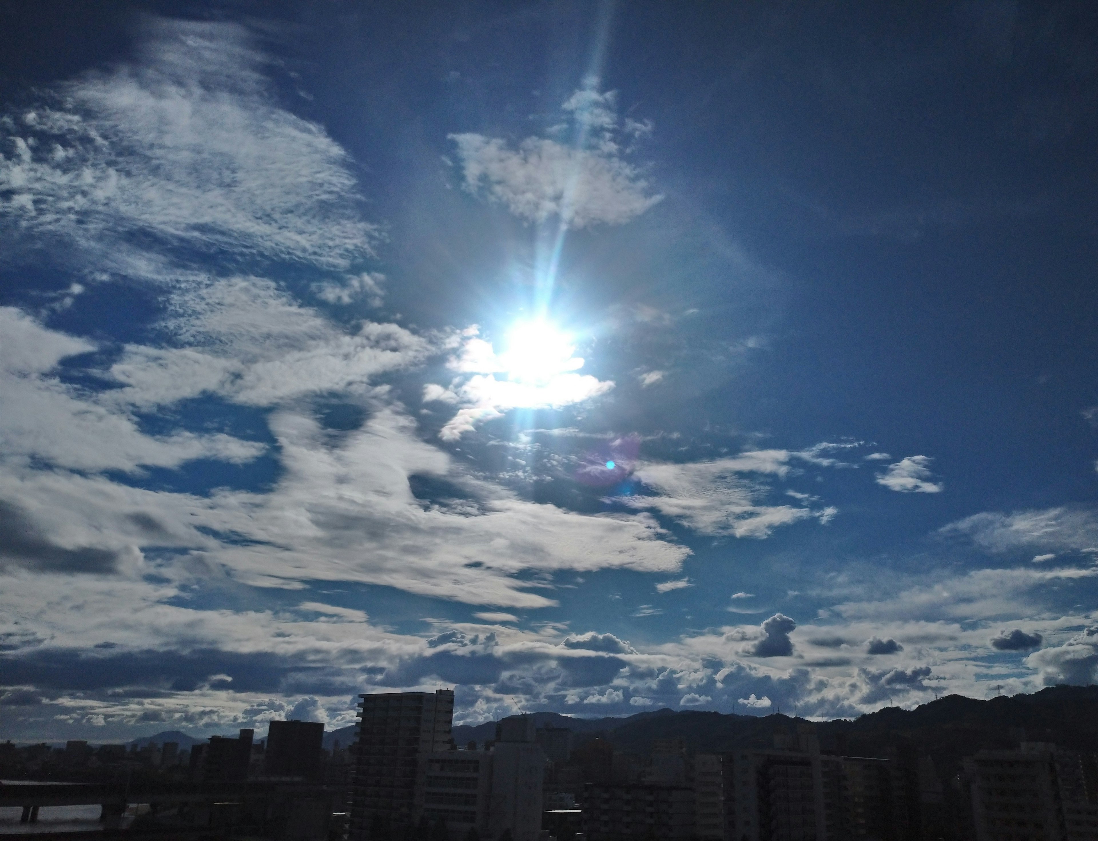 青空と白い雲の間に輝く太陽