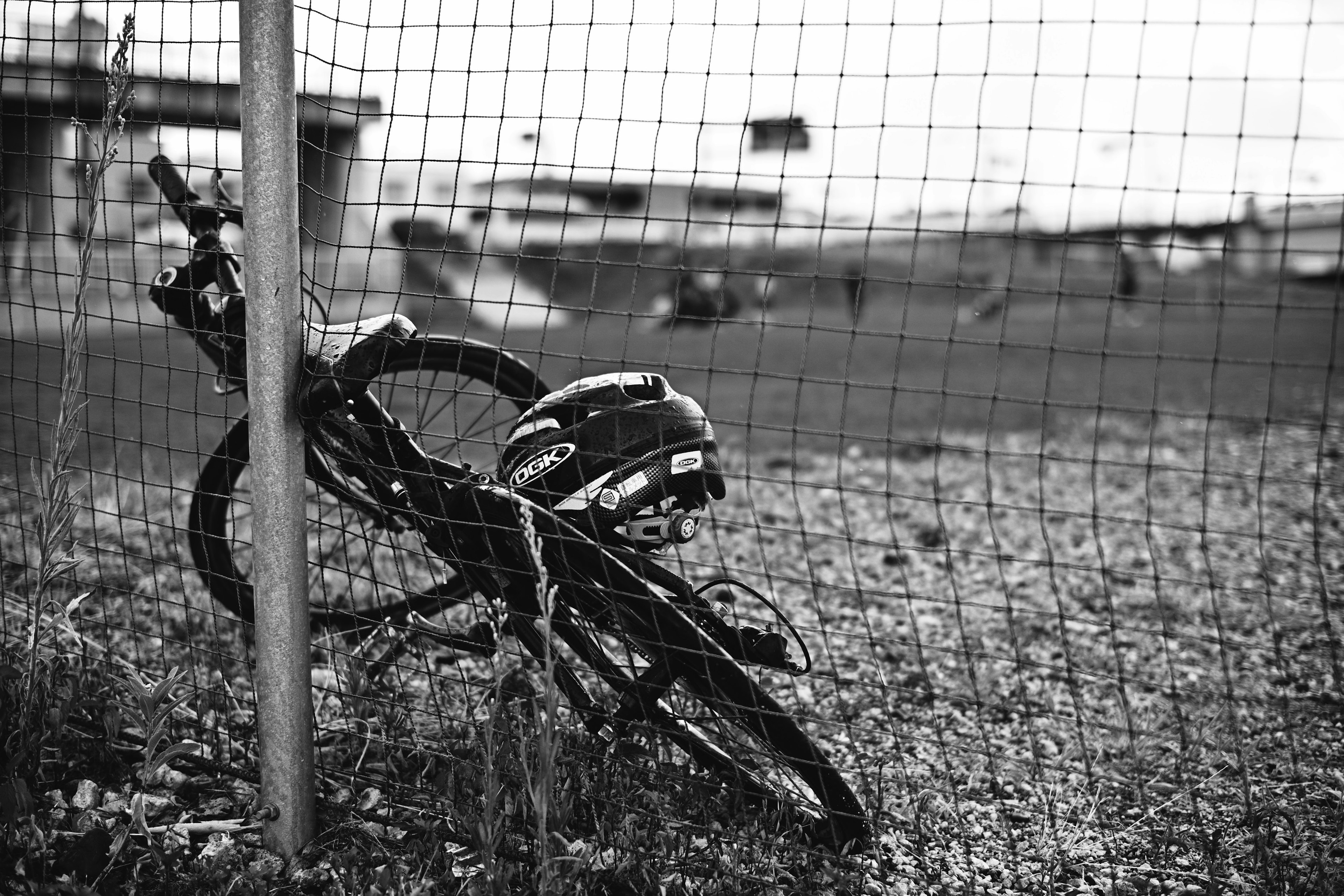 フェンスに寄りかかる黒い自転車とヘルメットのモノクロ画像