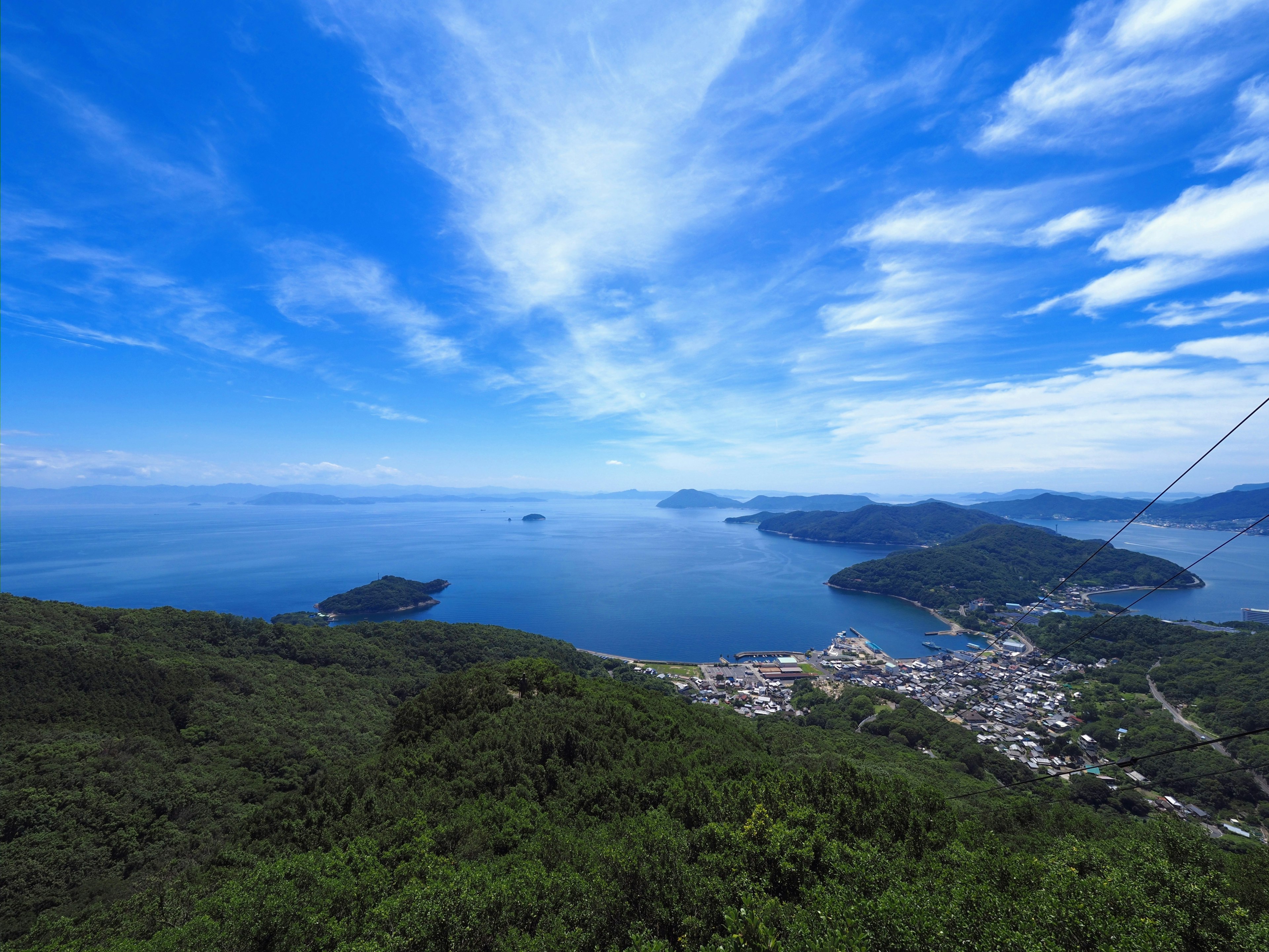 Una vista panorámica desde la cima de una montaña que muestra un mar y un cielo azules con islas dispersas y un pueblo visible