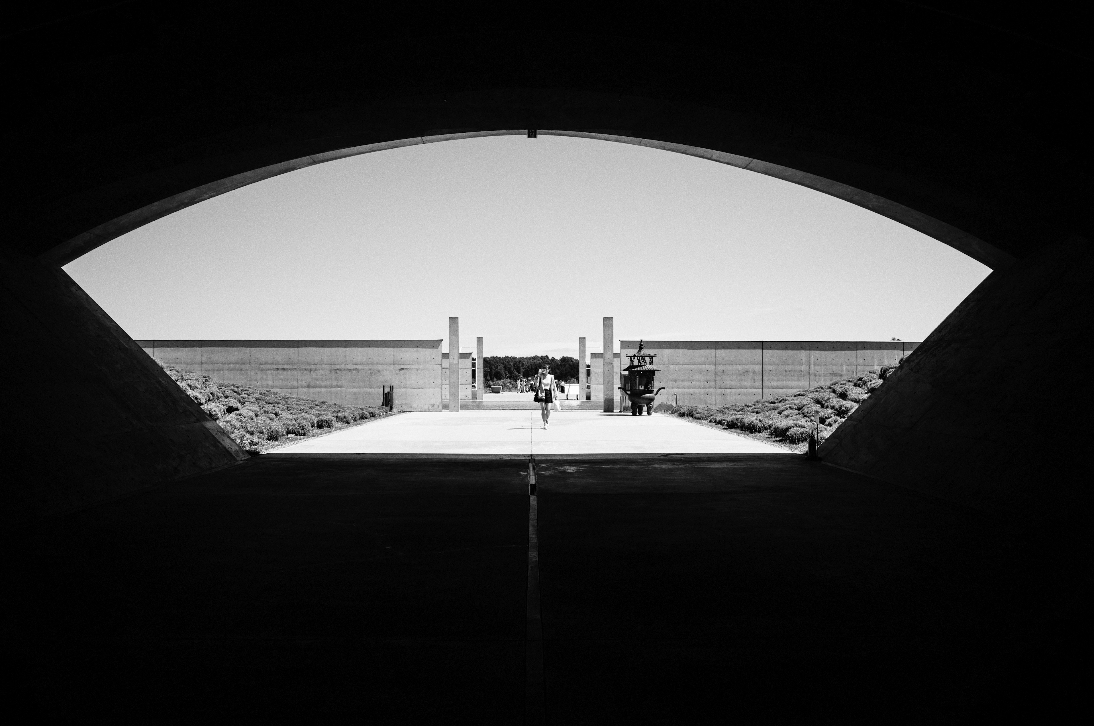 A person walking along a pathway visible through an arch-shaped opening in a black and white landscape