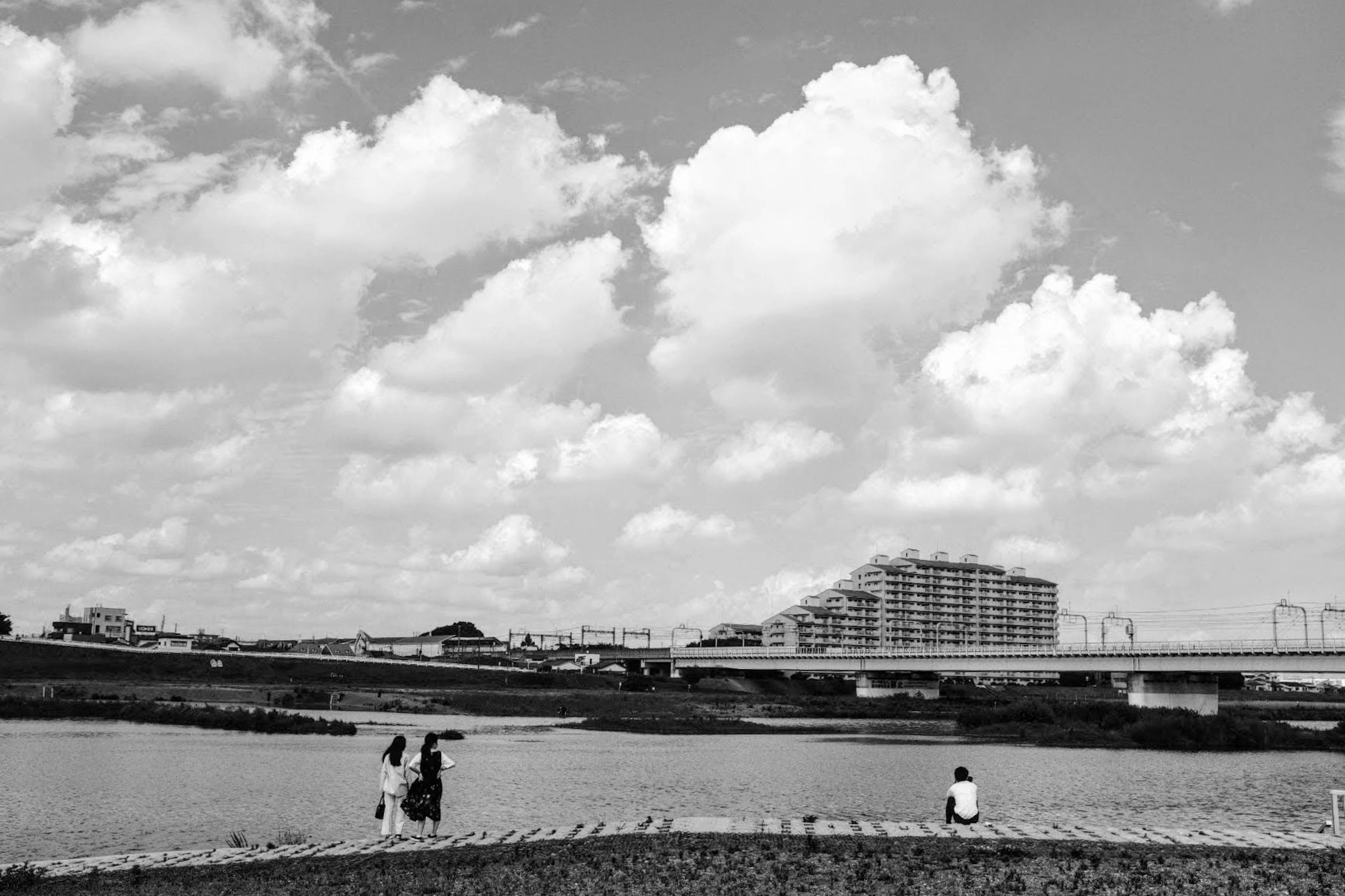 白黒の風景に川と高層ビルが映る空の下で人々が座っている