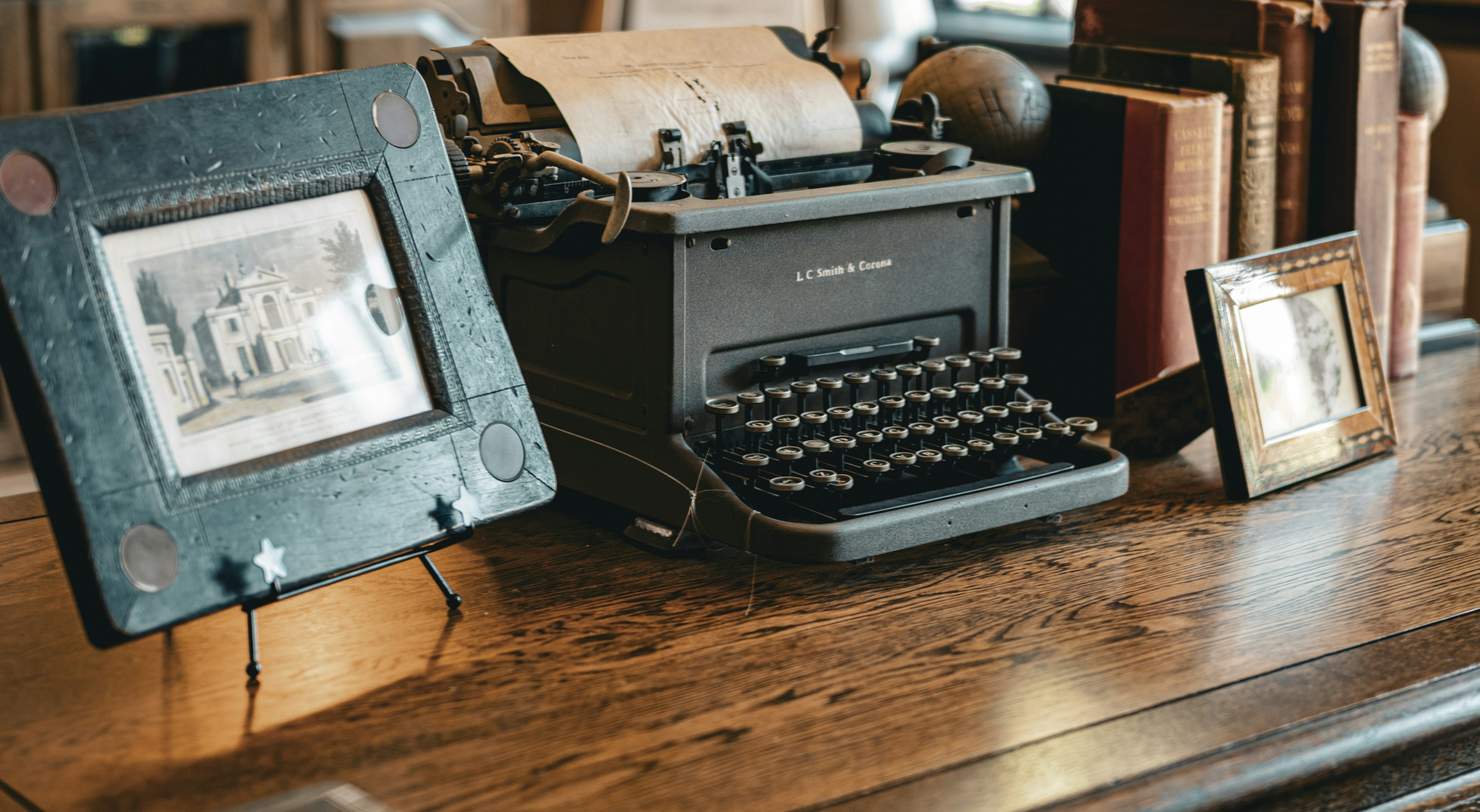 An antique typewriter on a wooden table with framed photographs nearby