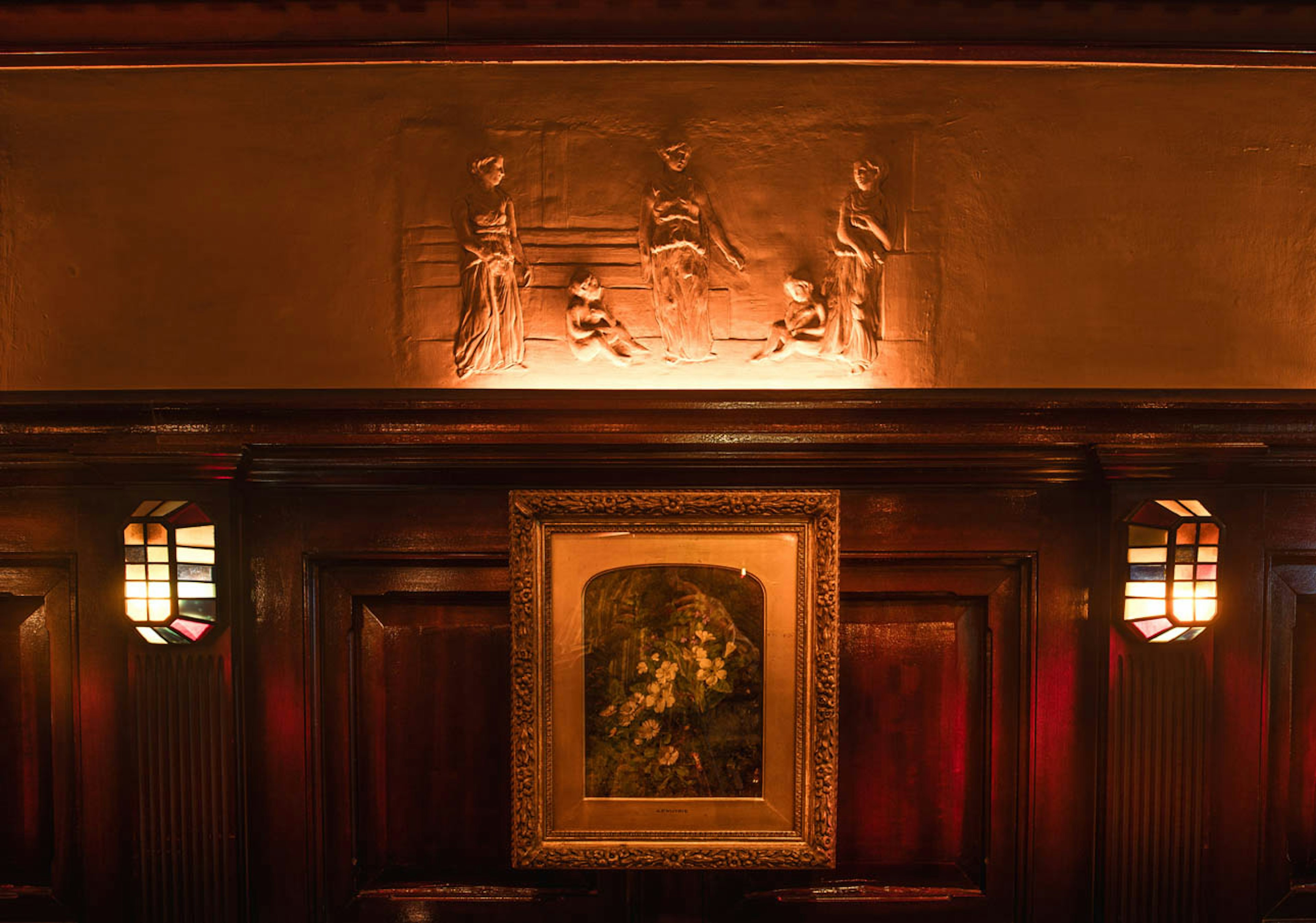 Wooden wall with warm lighting featuring a bas-relief and a framed painting