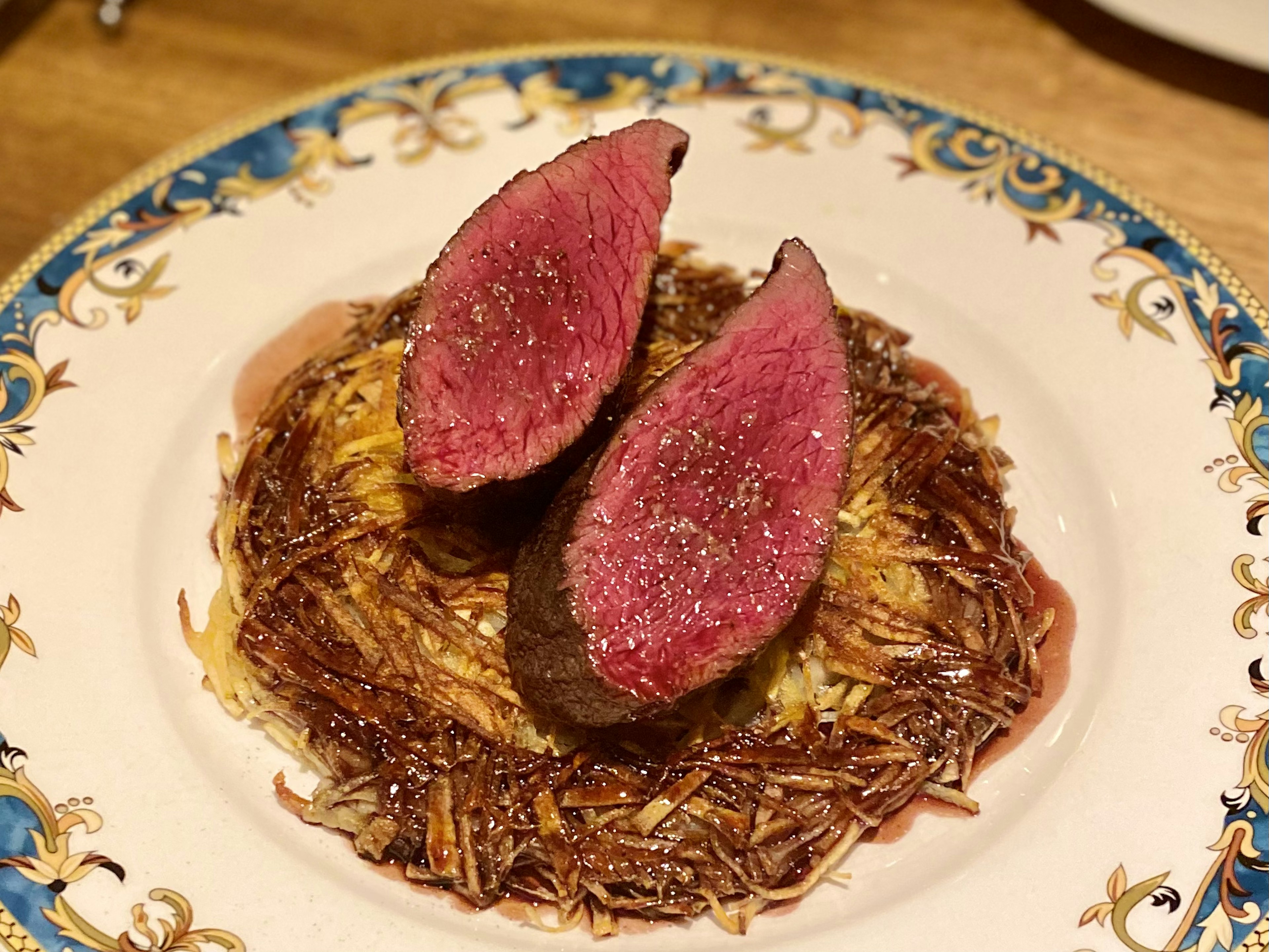 Hidangan yang disajikan dengan indah menampilkan dua irisan daging merah muda di atas dasar renyah