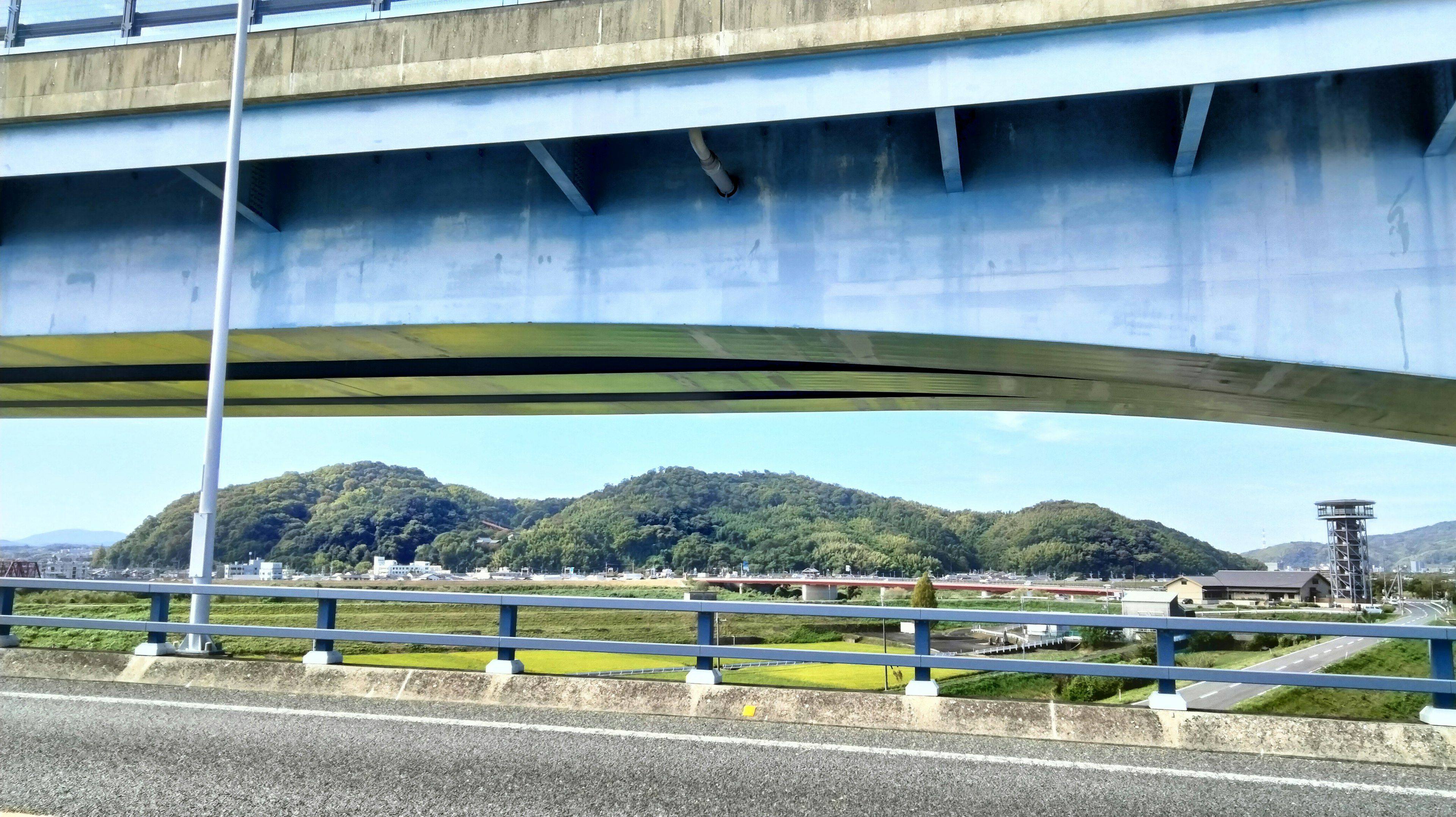 Blick auf grüne Hügel und ländliche Landschaft von unter einer blauen Brücke