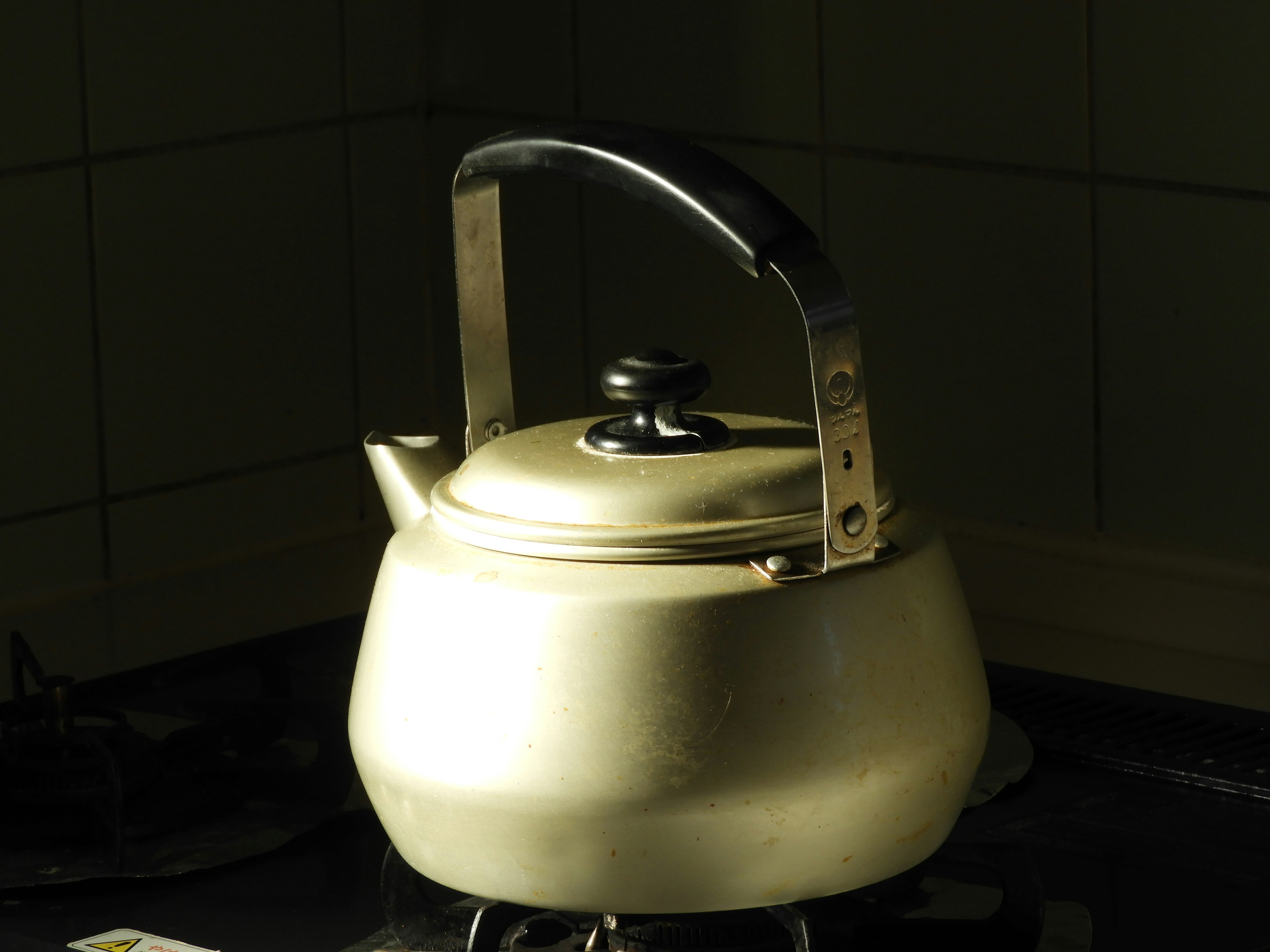 A simple metal kettle on a kitchen stove with soft lighting