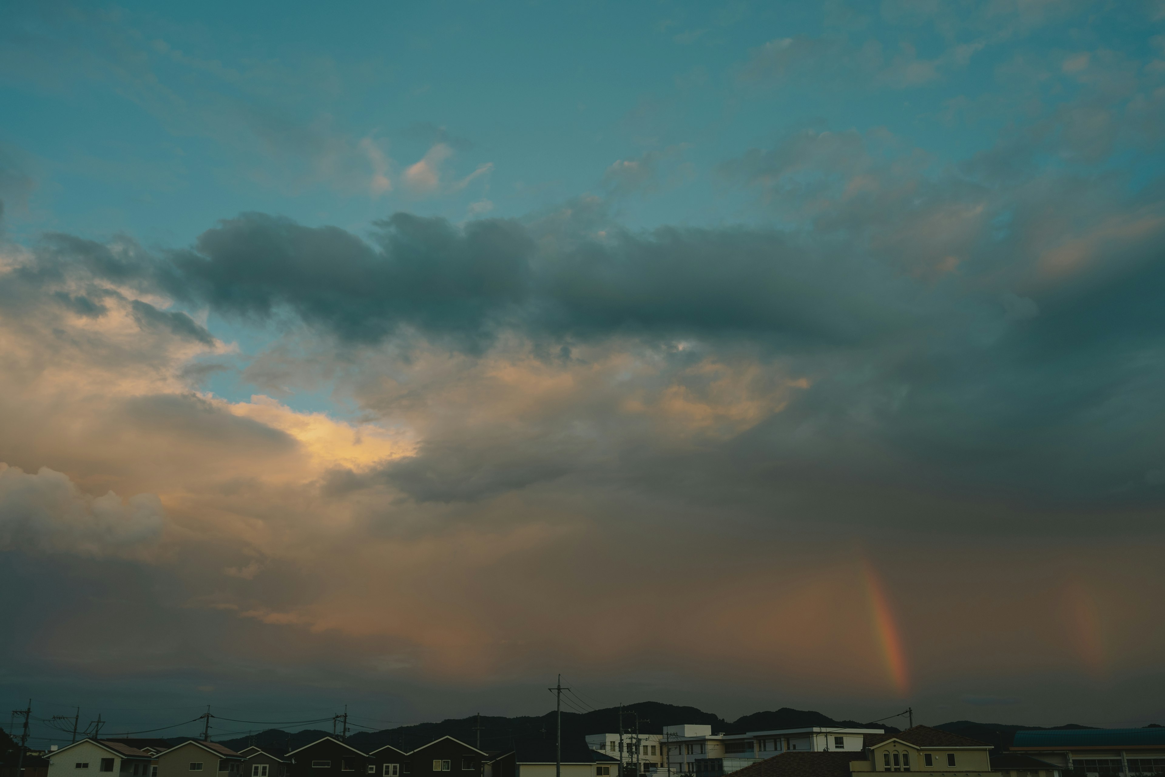 Cielo nublado con un arcoíris sobre una zona residencial