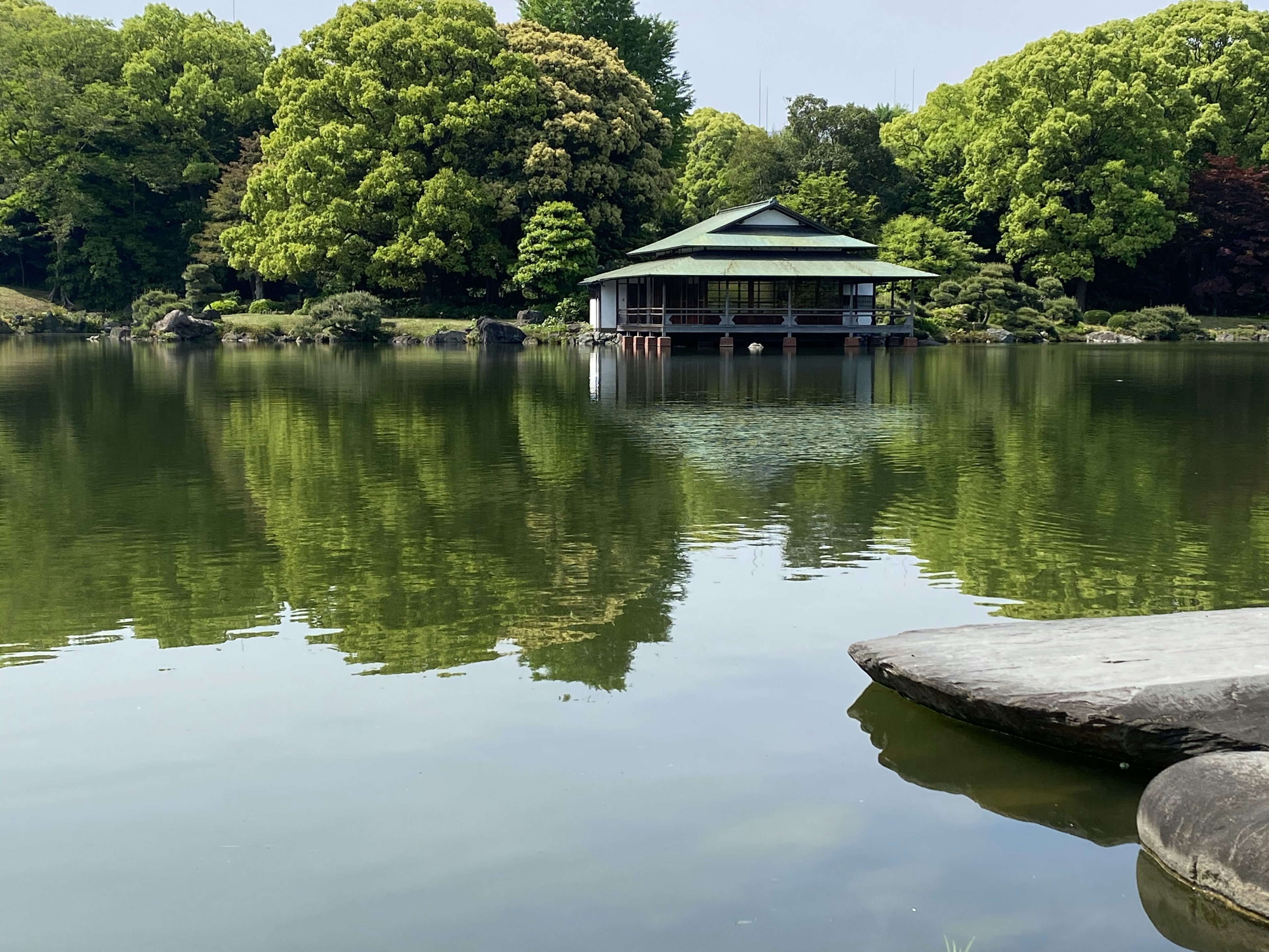 Traditional Japanese building by a serene pond surrounded by lush green trees