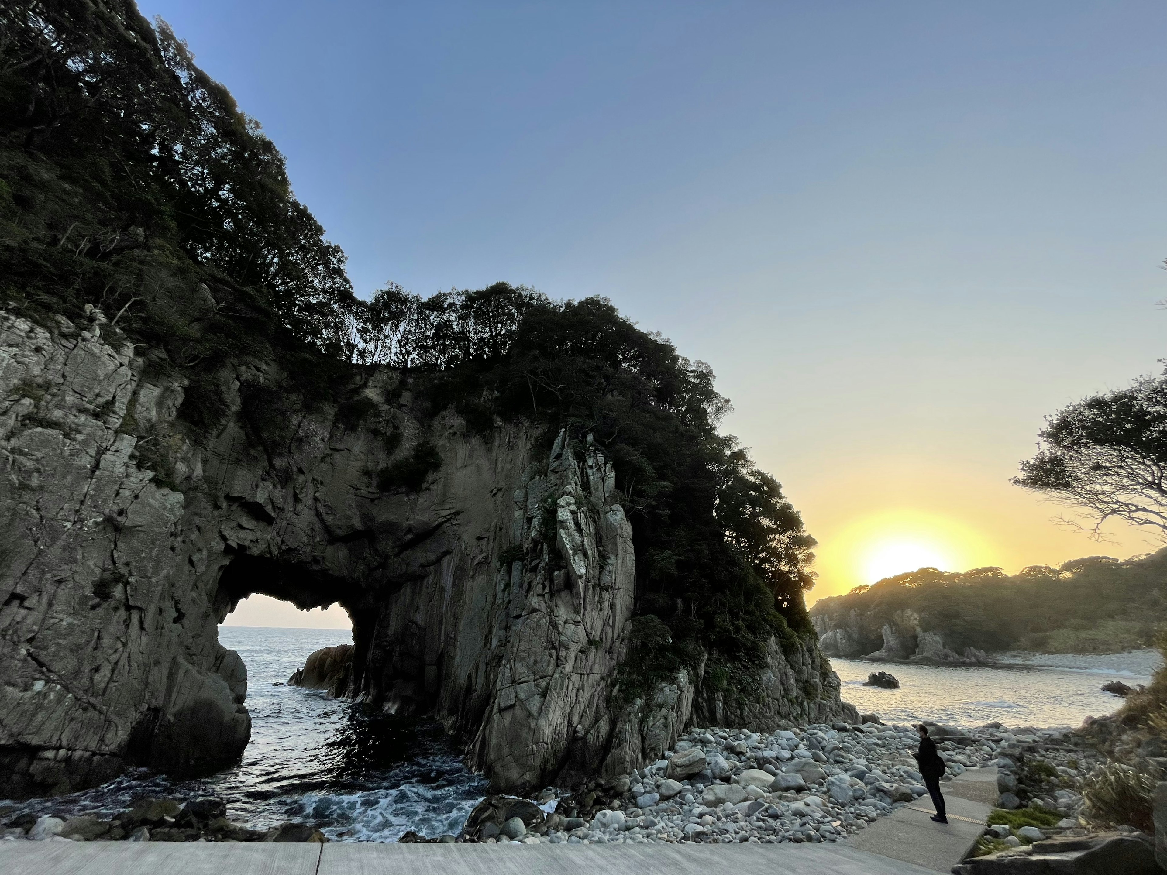 夕日を背にした岩のアーチと海岸の風景