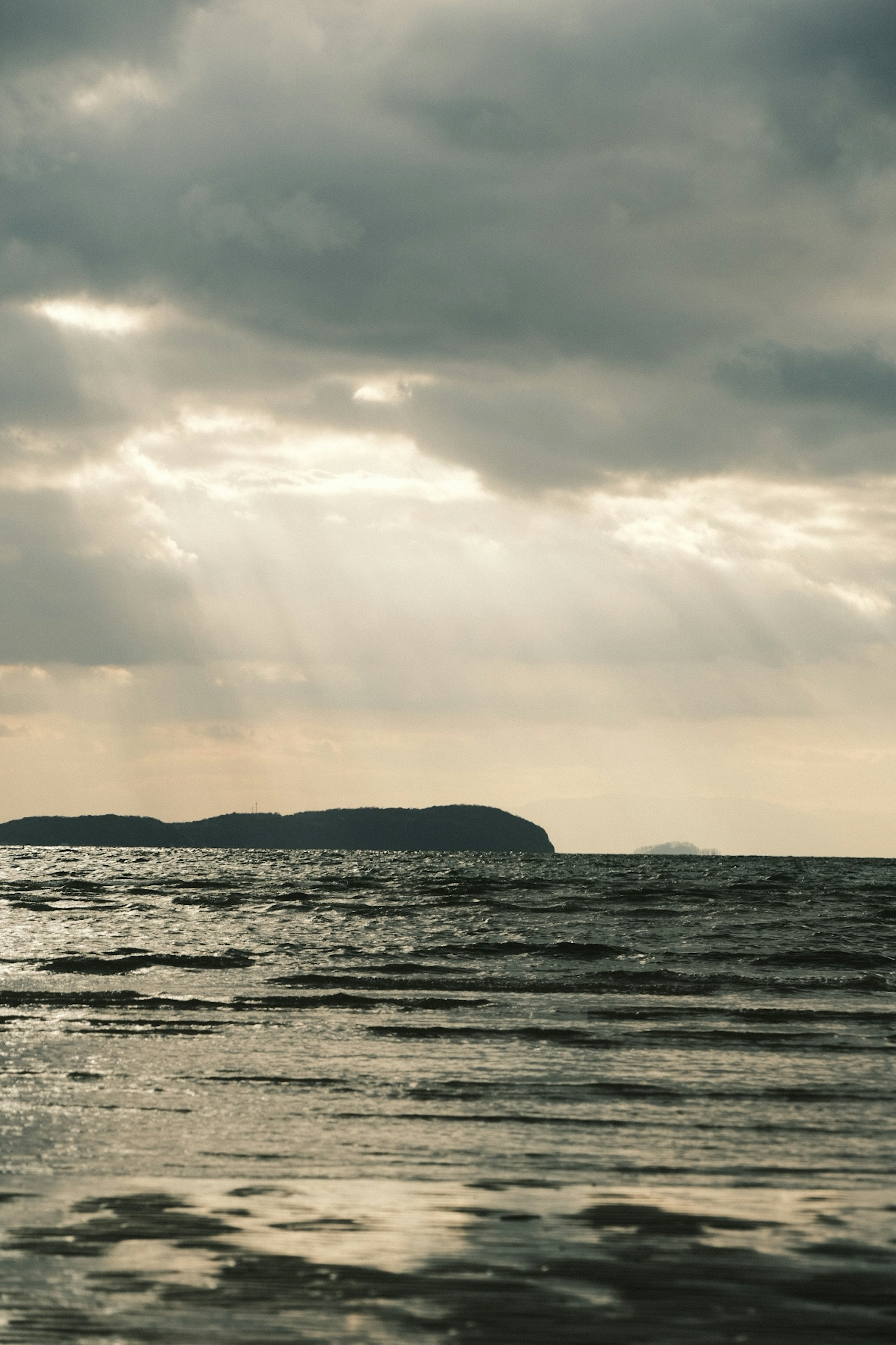 Pemandangan laut tenang dengan langit mendung dan pulau jauh