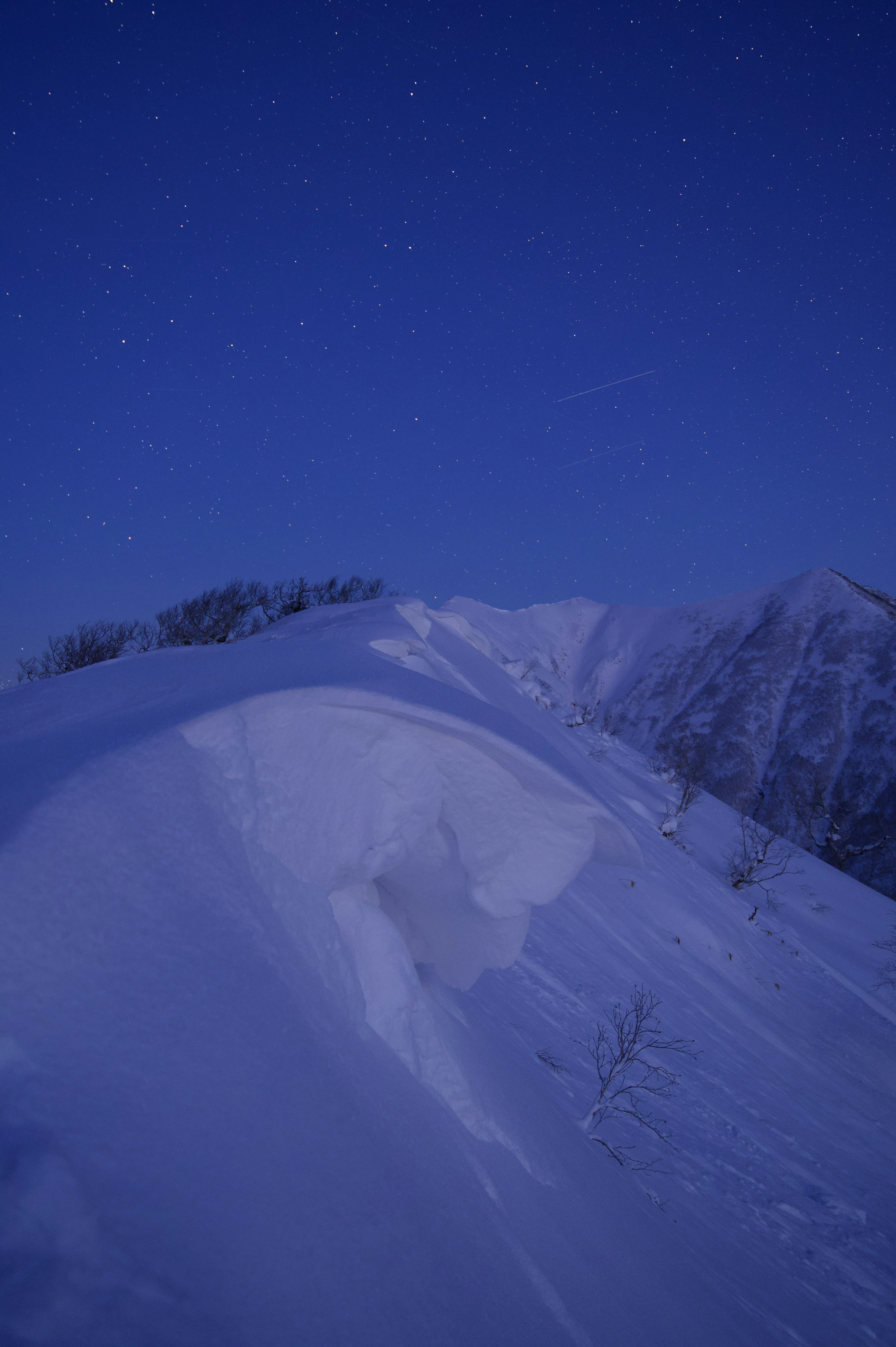 Paesaggio montano innevato sotto un cielo stellato con curve di neve morbide e tonalità blu freddo