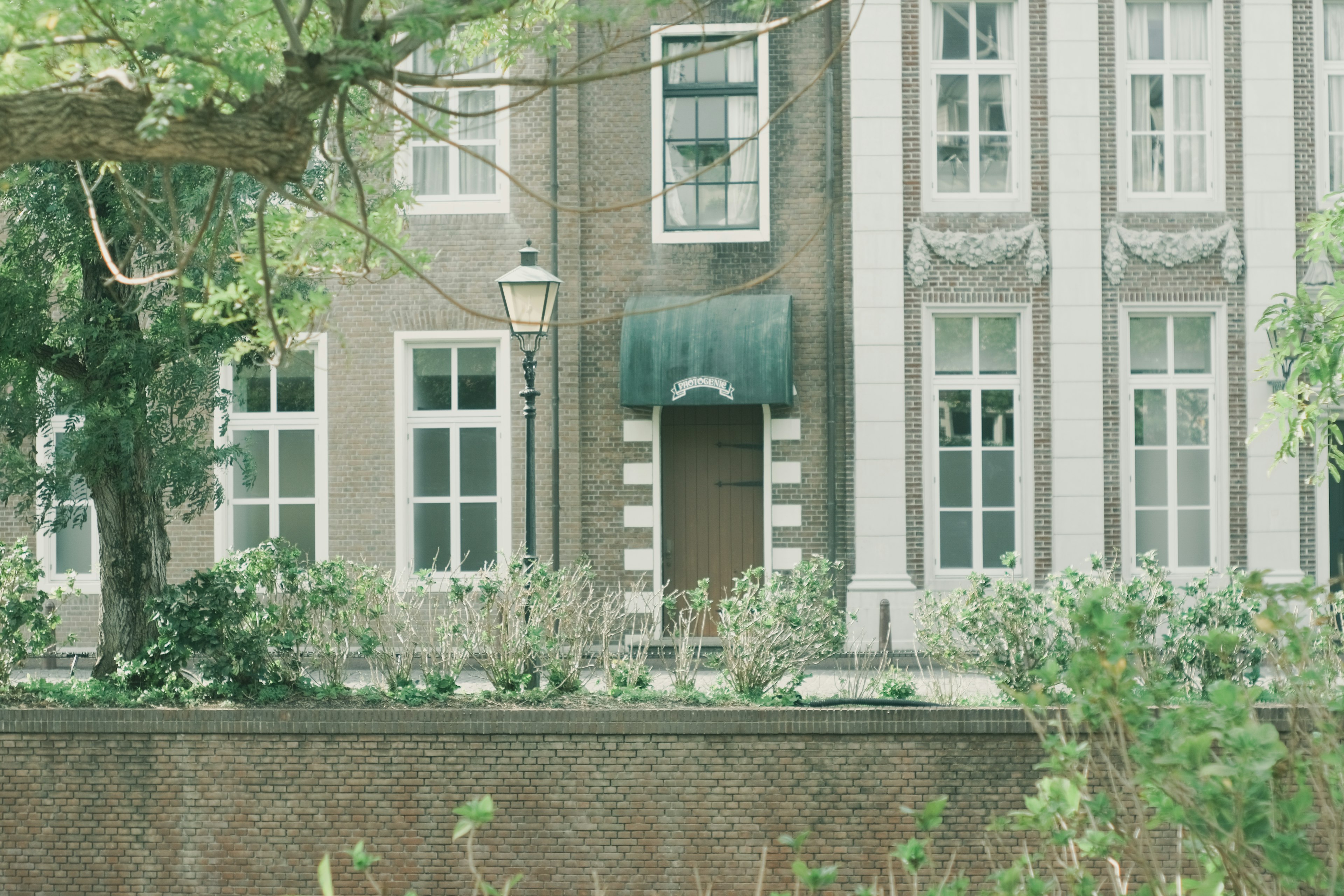 Façade d'un vieux bâtiment entouré de plantes vertes, avec des fenêtres blanches et un auvent vert