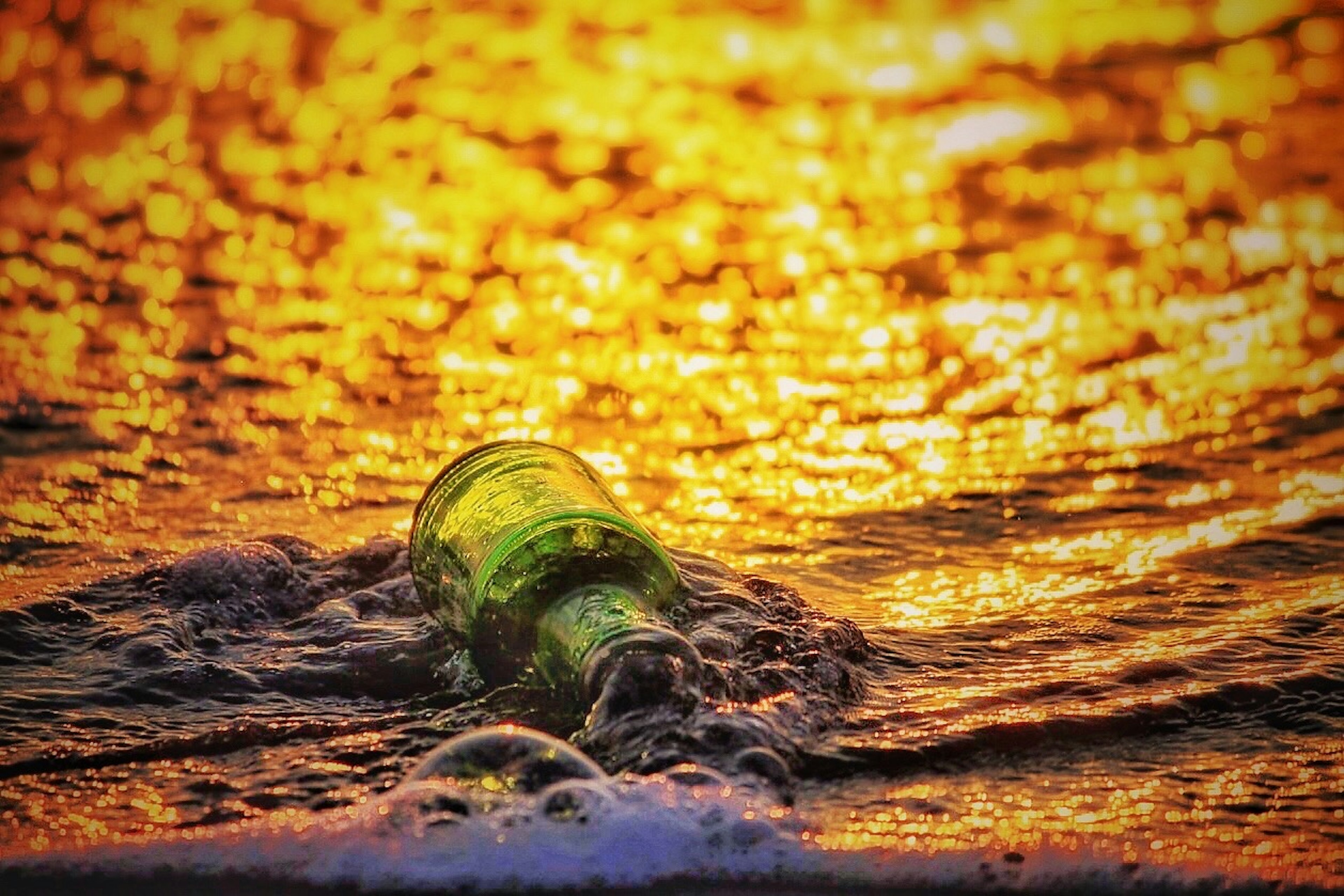 Grüne Flasche in den Wellen mit Sonnenuntergangsreflexionen