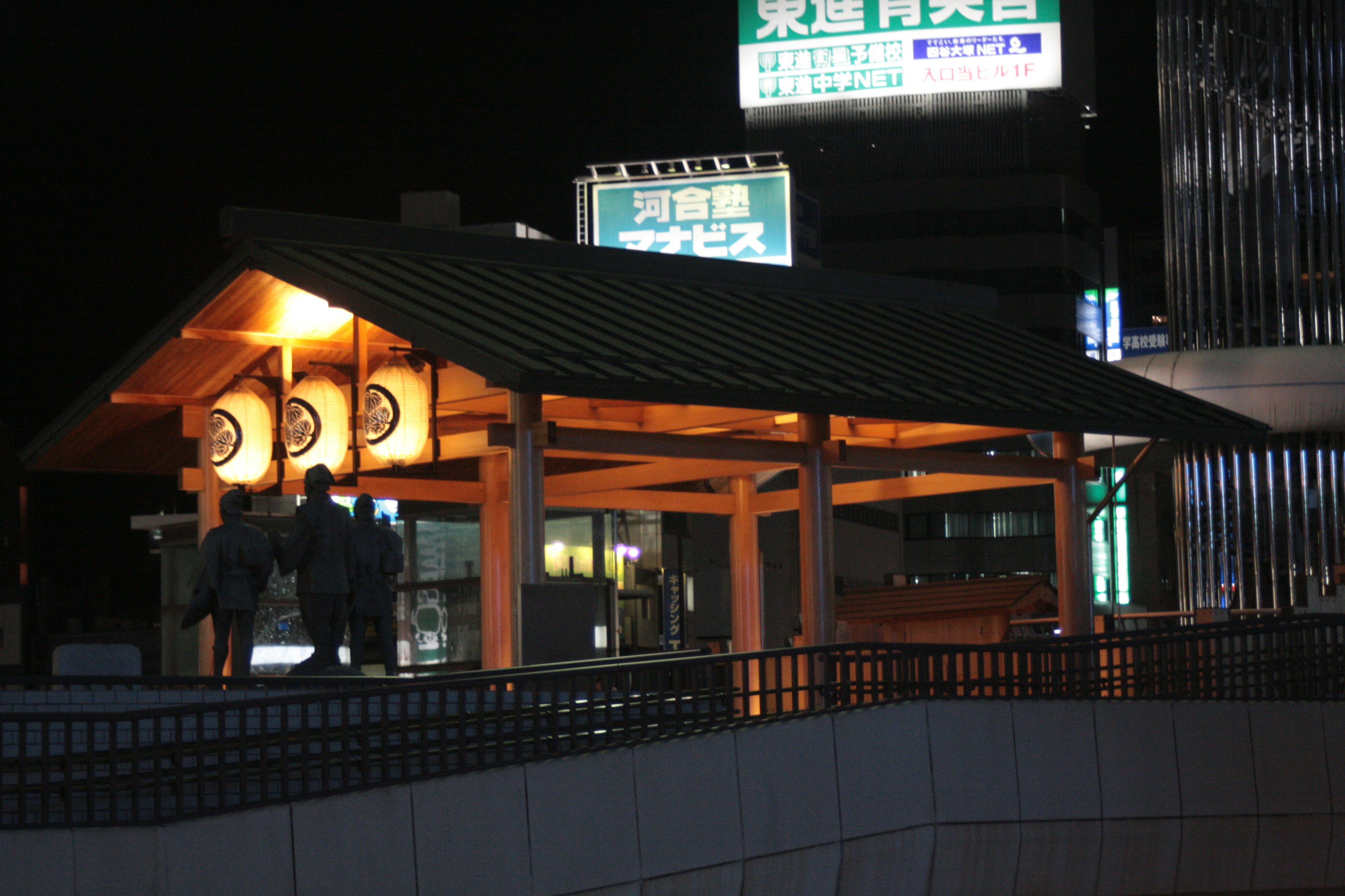 Night view of a roofed waiting area at a station with signage