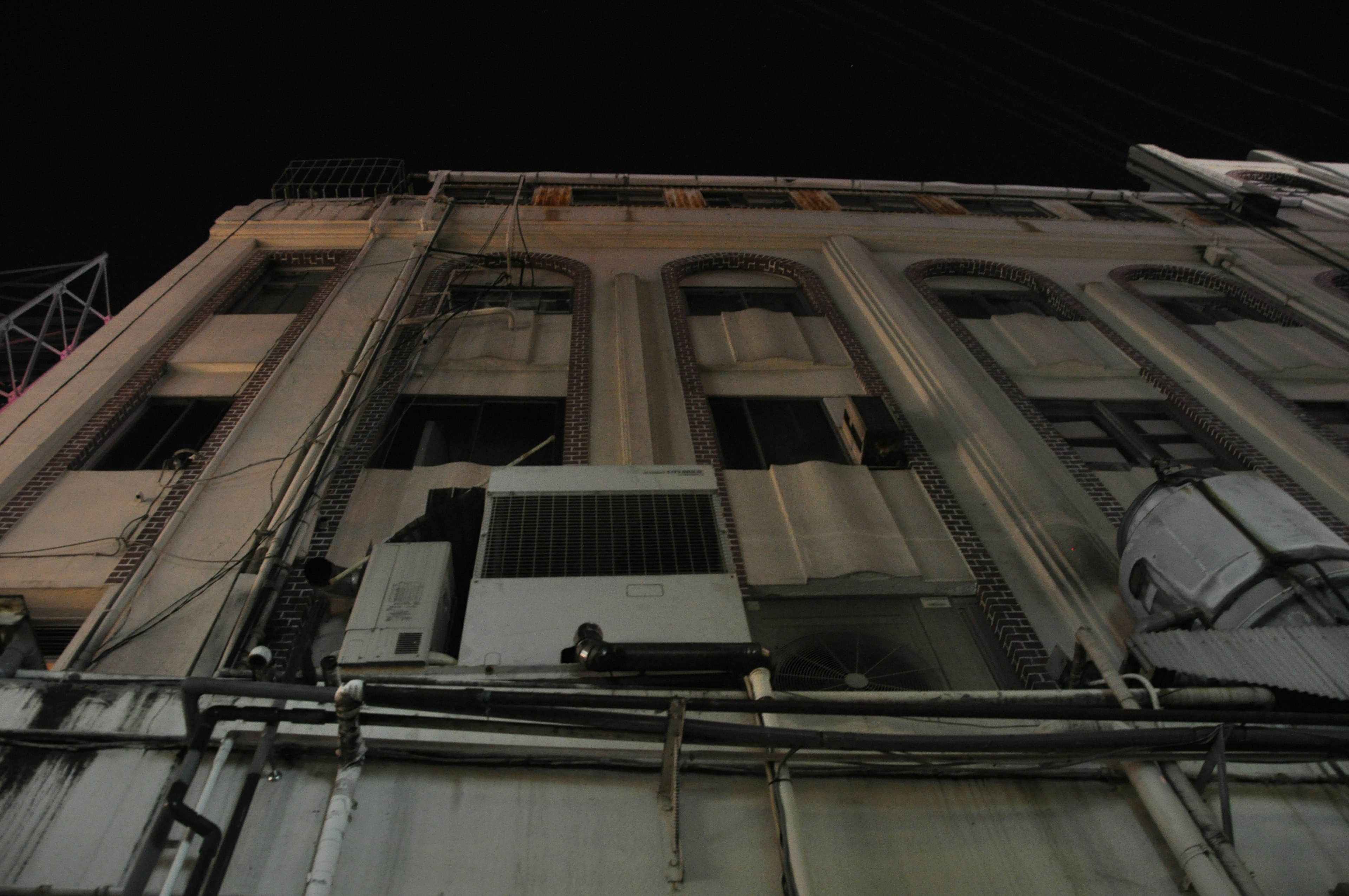 Vista nocturna de una pared de edificio con unidades de aire acondicionado visibles