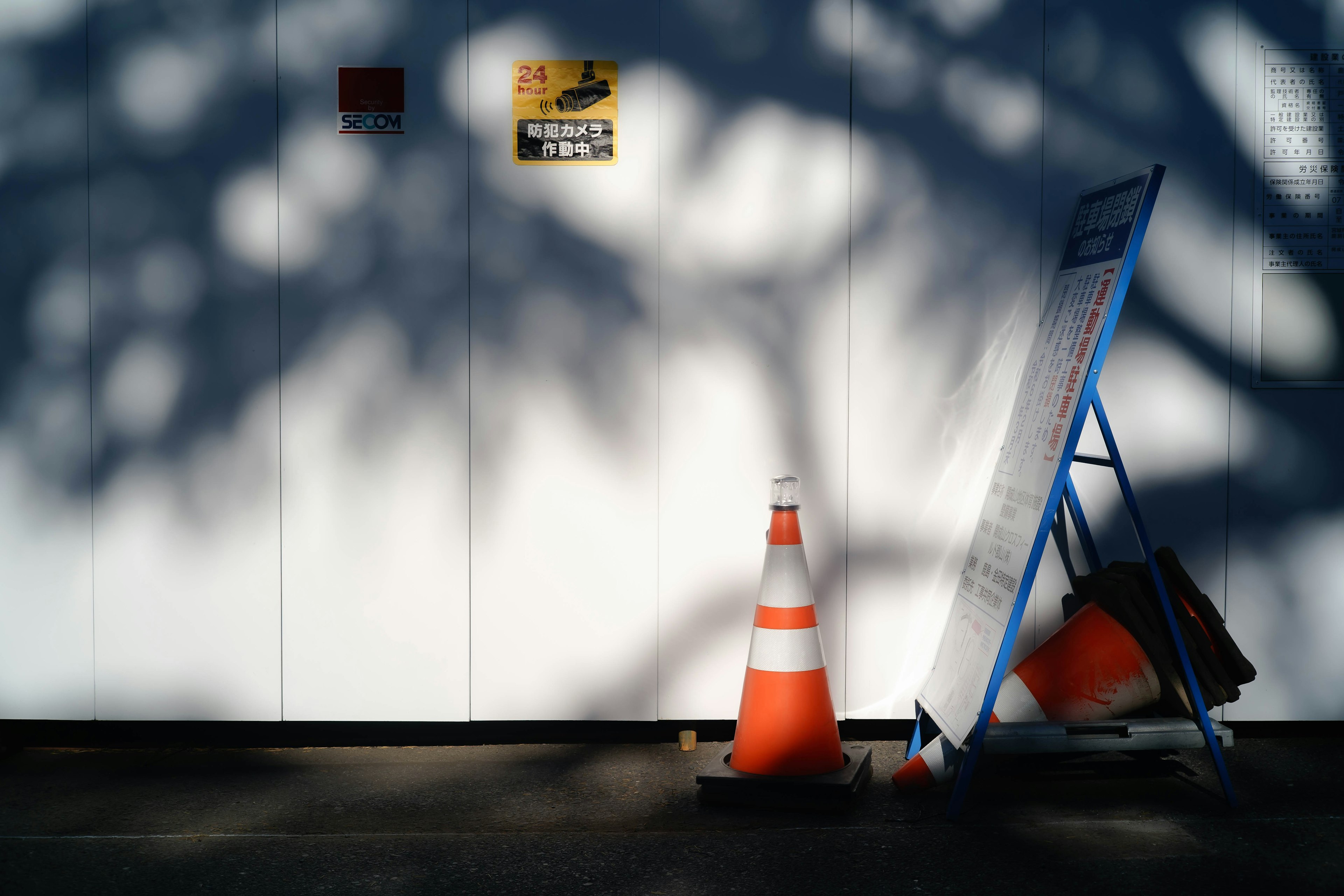 Cono de tráfico naranja y cartel azul contra una pared blanca con sombras