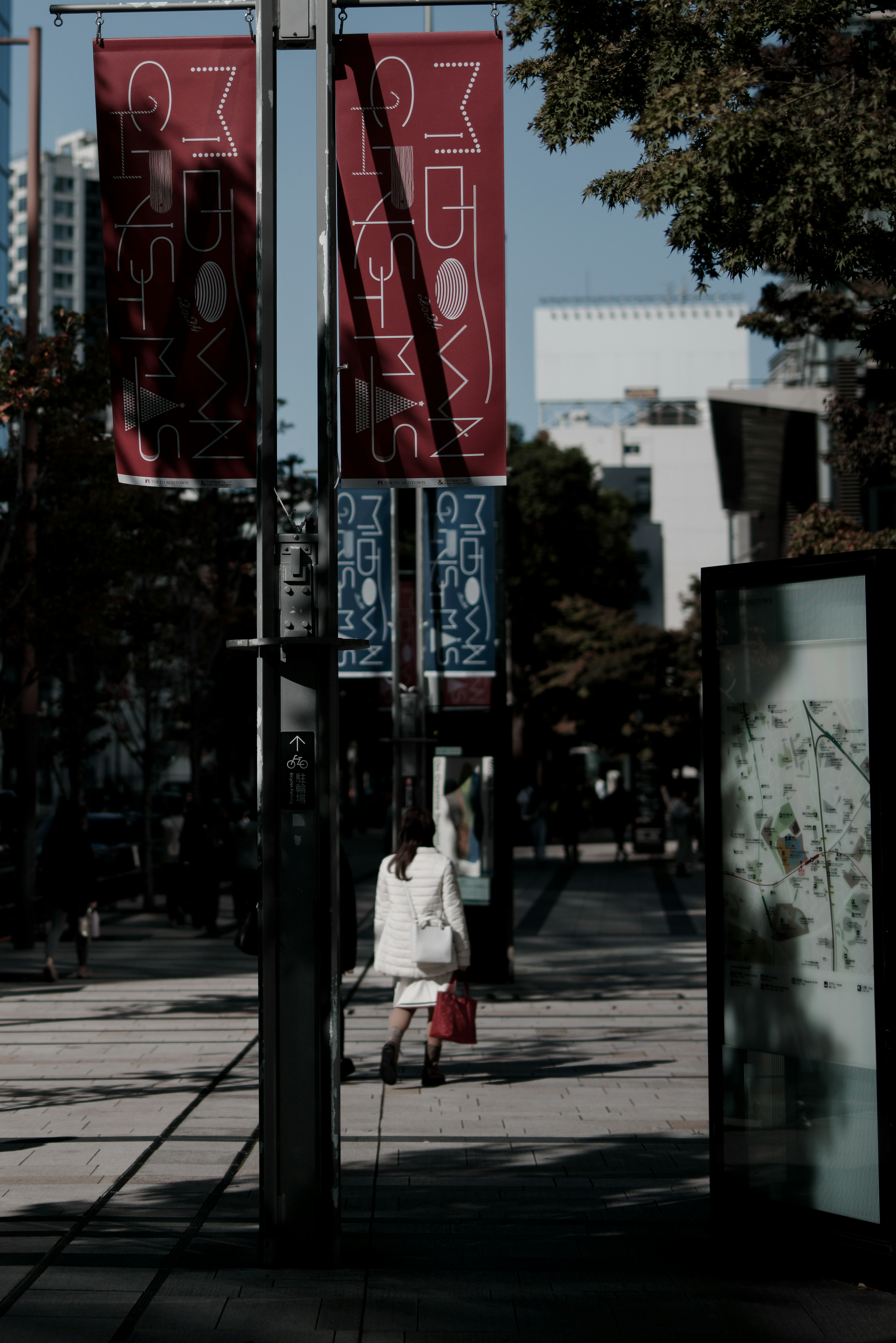 白い服を着た人物が通りを歩いているシーン 赤いと青いバナーが目立つ 都市の風景