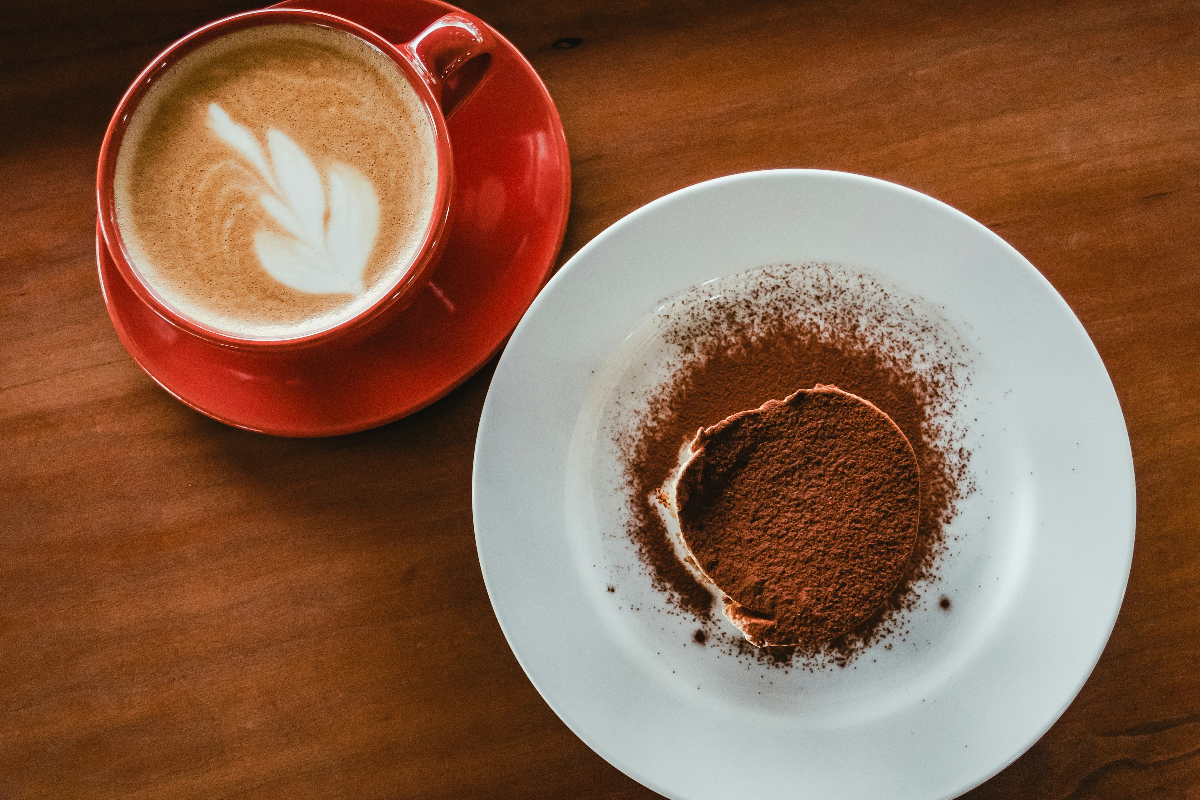 Eine rote Tasse mit Latte Art neben einem Schokoladendessert auf einem weißen Teller