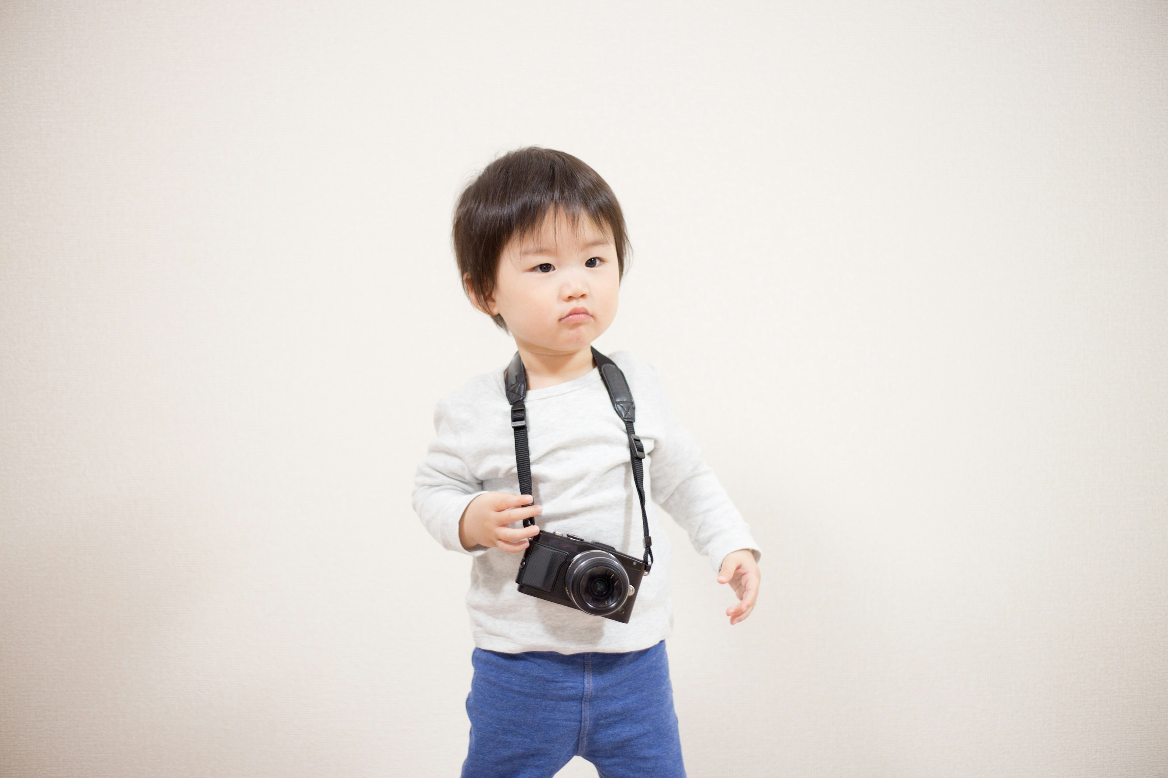 Bambino in piedi con una macchina fotografica al collo su uno sfondo semplice