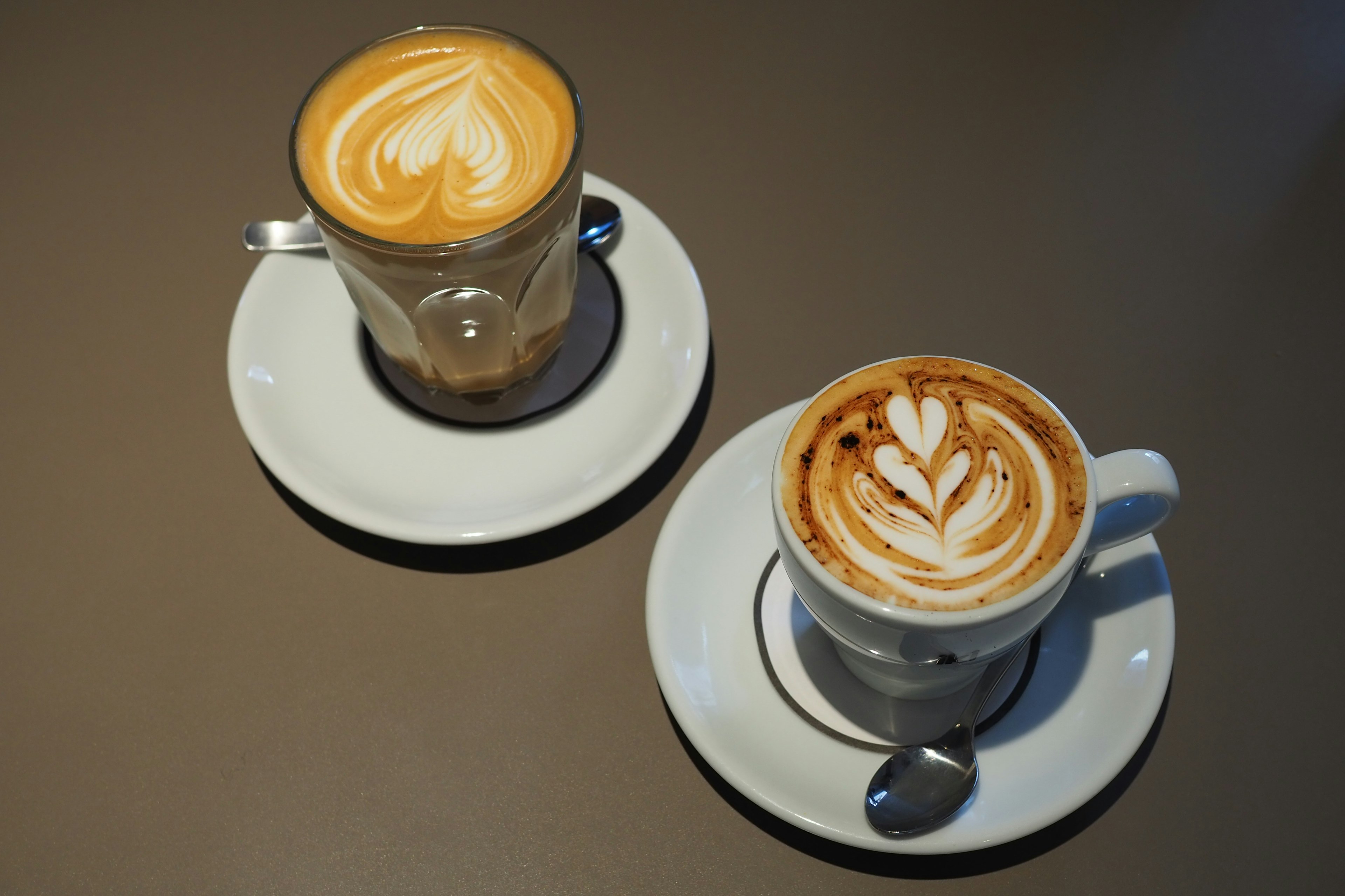 Two lattes presented on a table one in a clear glass and the other in a white cup with latte art