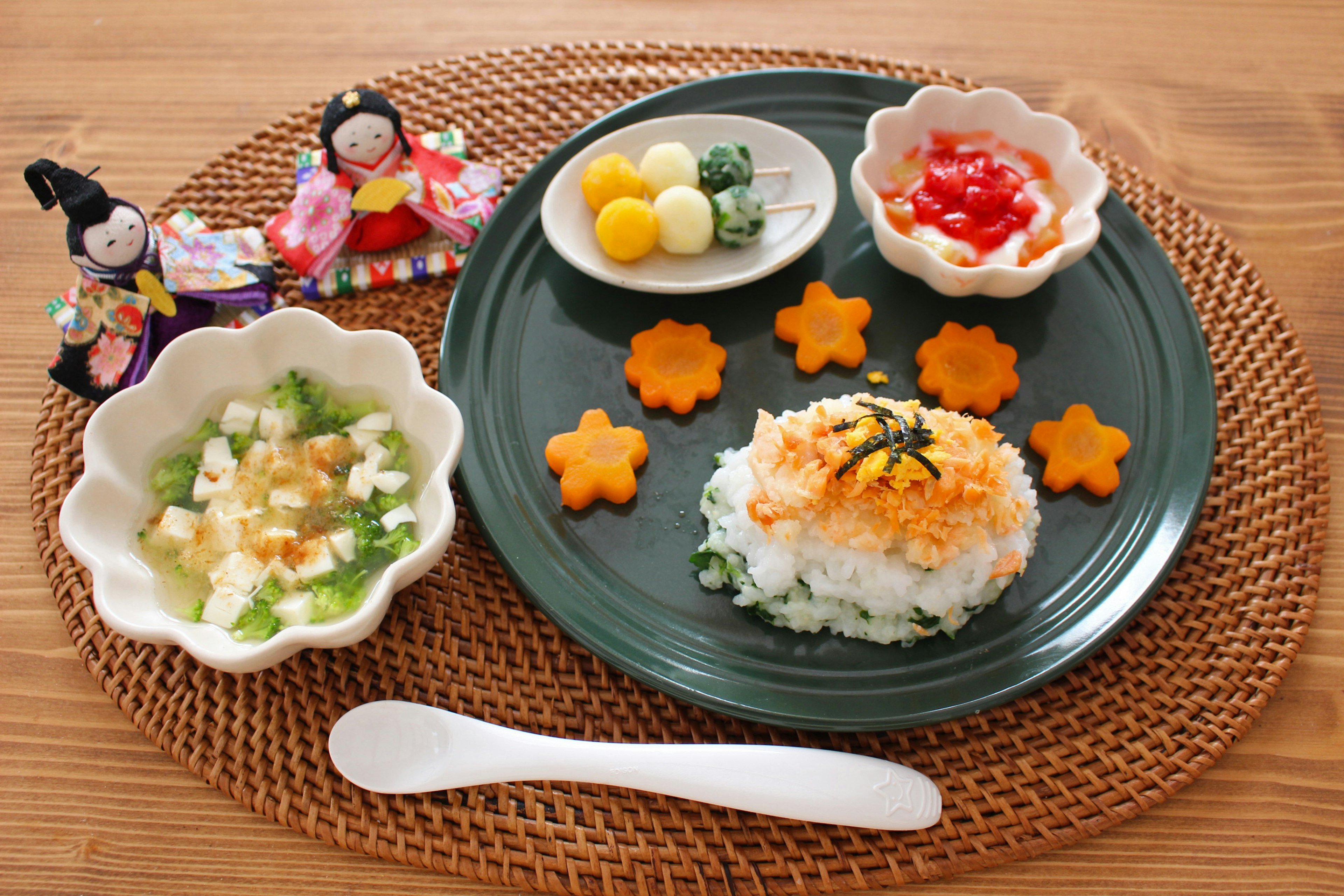 A beautifully arranged Japanese meal with colorful dishes and traditional hina dolls displayed