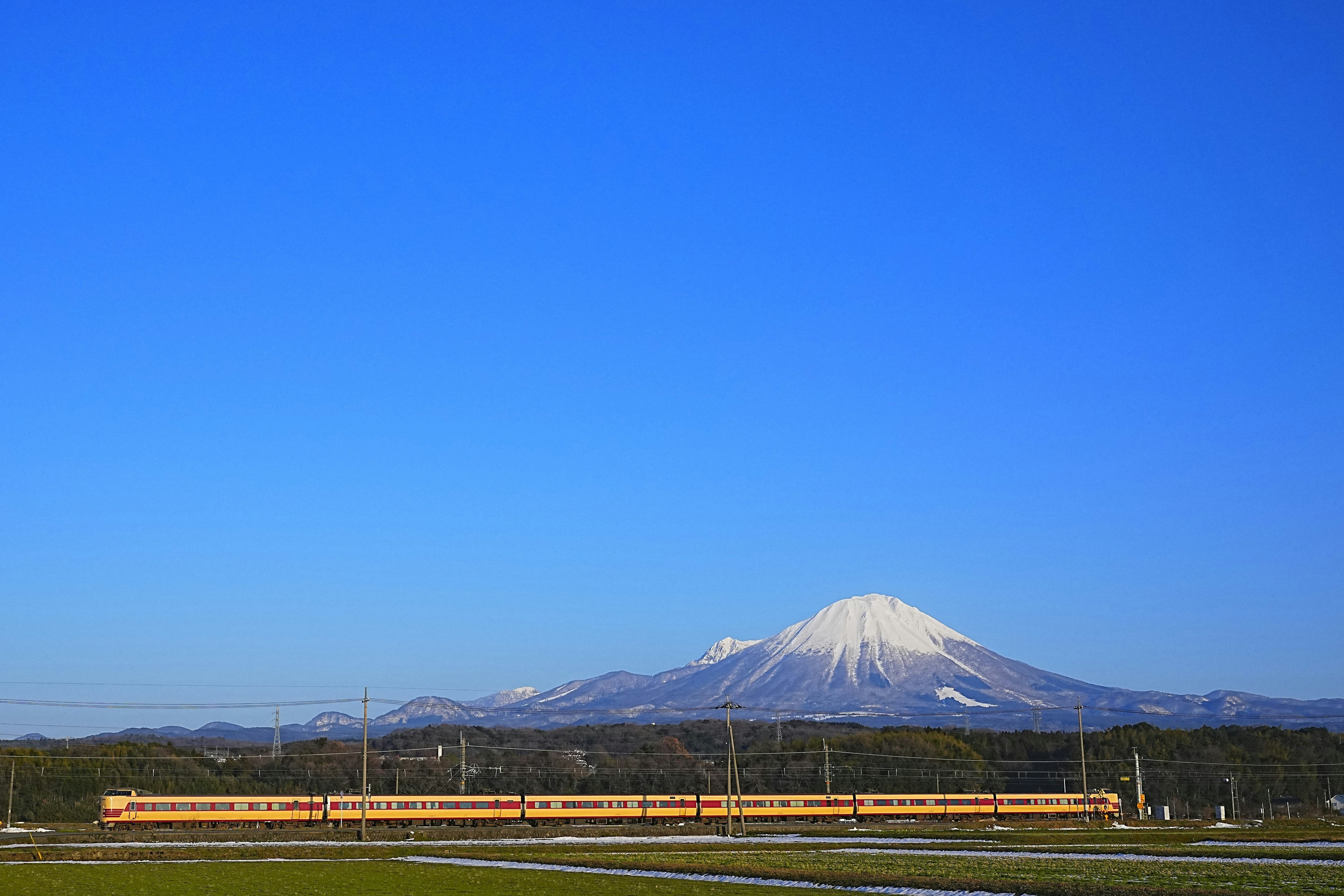 青空の下に雪をかぶった山と黄色い列車