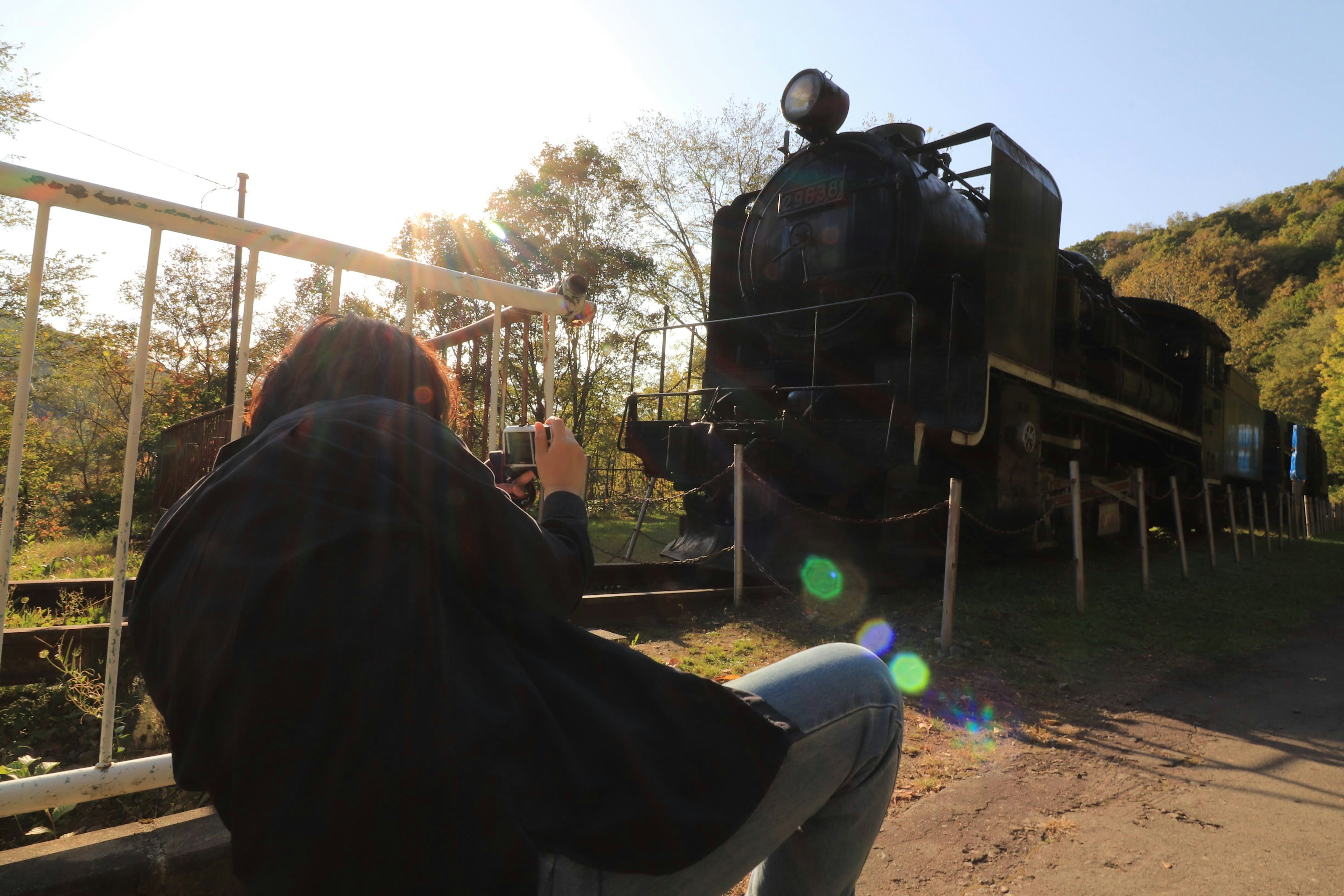 Silhouette of a person taking a photo in front of an old steam locomotive with bright natural light