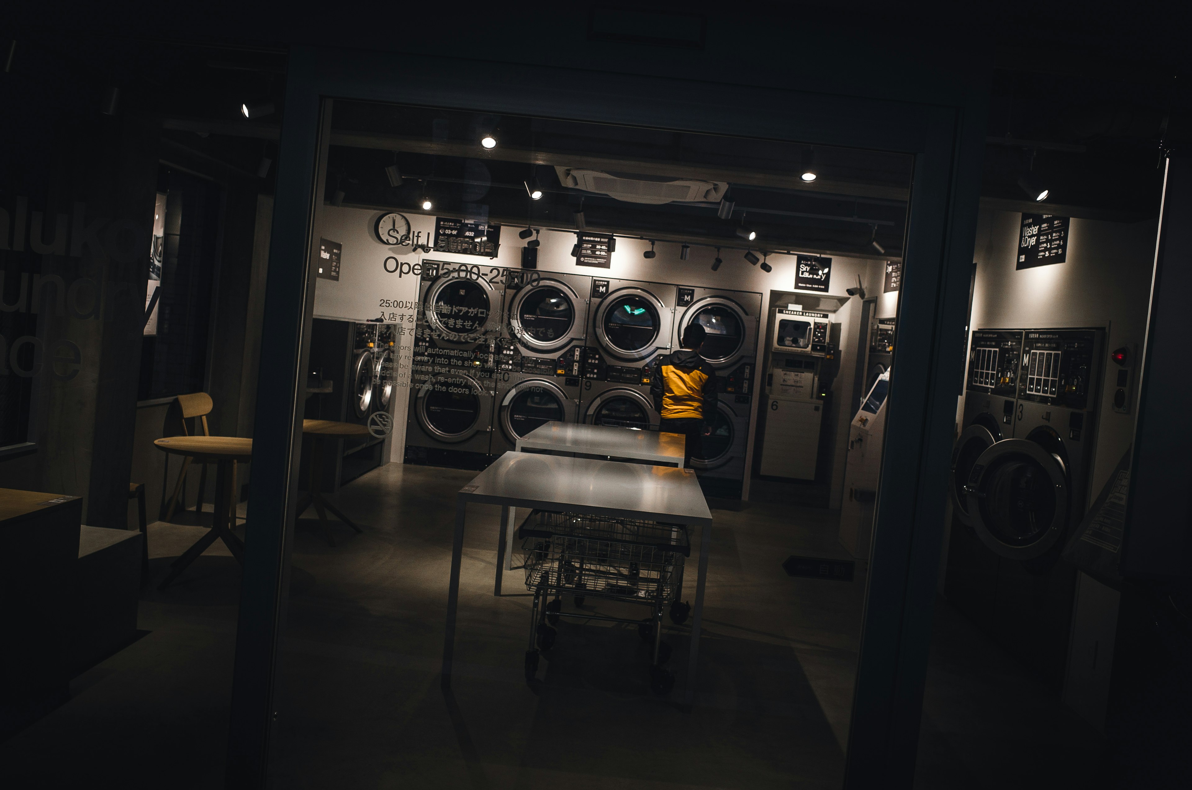 Intérieur d'une laverie sombre avec des rangées de machines à laver et une personne